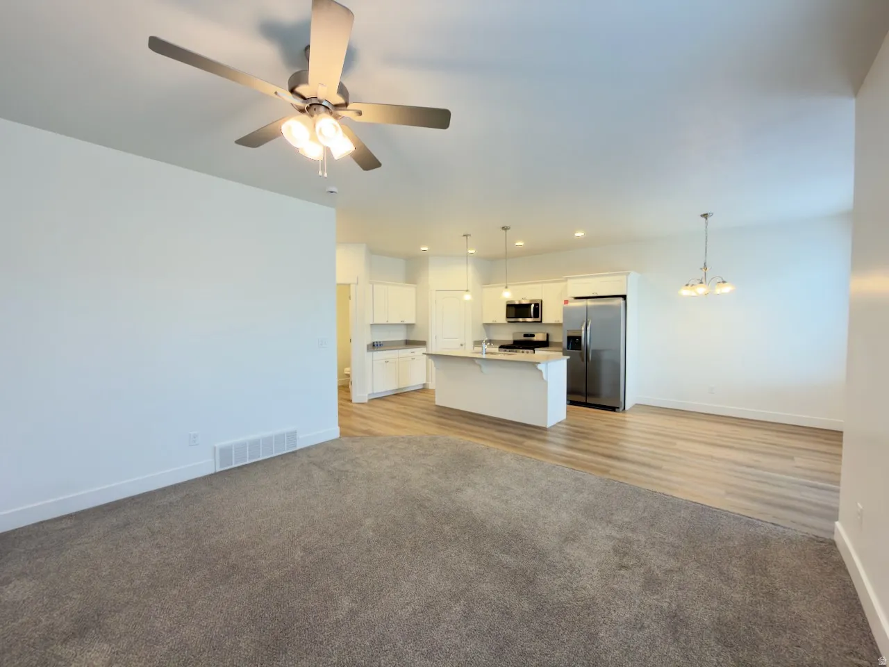 Open-concept living space with a ceiling fan, recessed lighting, and a kitchen featuring white cabinetry, stainless steel appliances, and a central island with pendant lighting