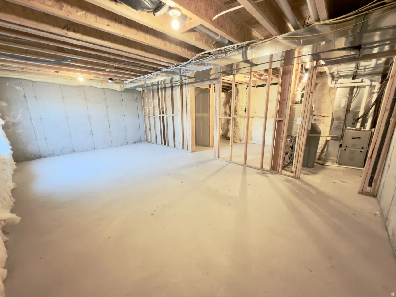 Unfinished basement space featuring concrete flooring, exposed ceiling joists, framed interior walls, visible ductwork, and mechanical systems