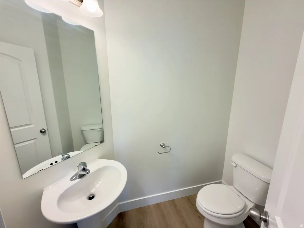 Powder room featuring a pedestal sink, wall-mounted mirror, and wood-finish flooring