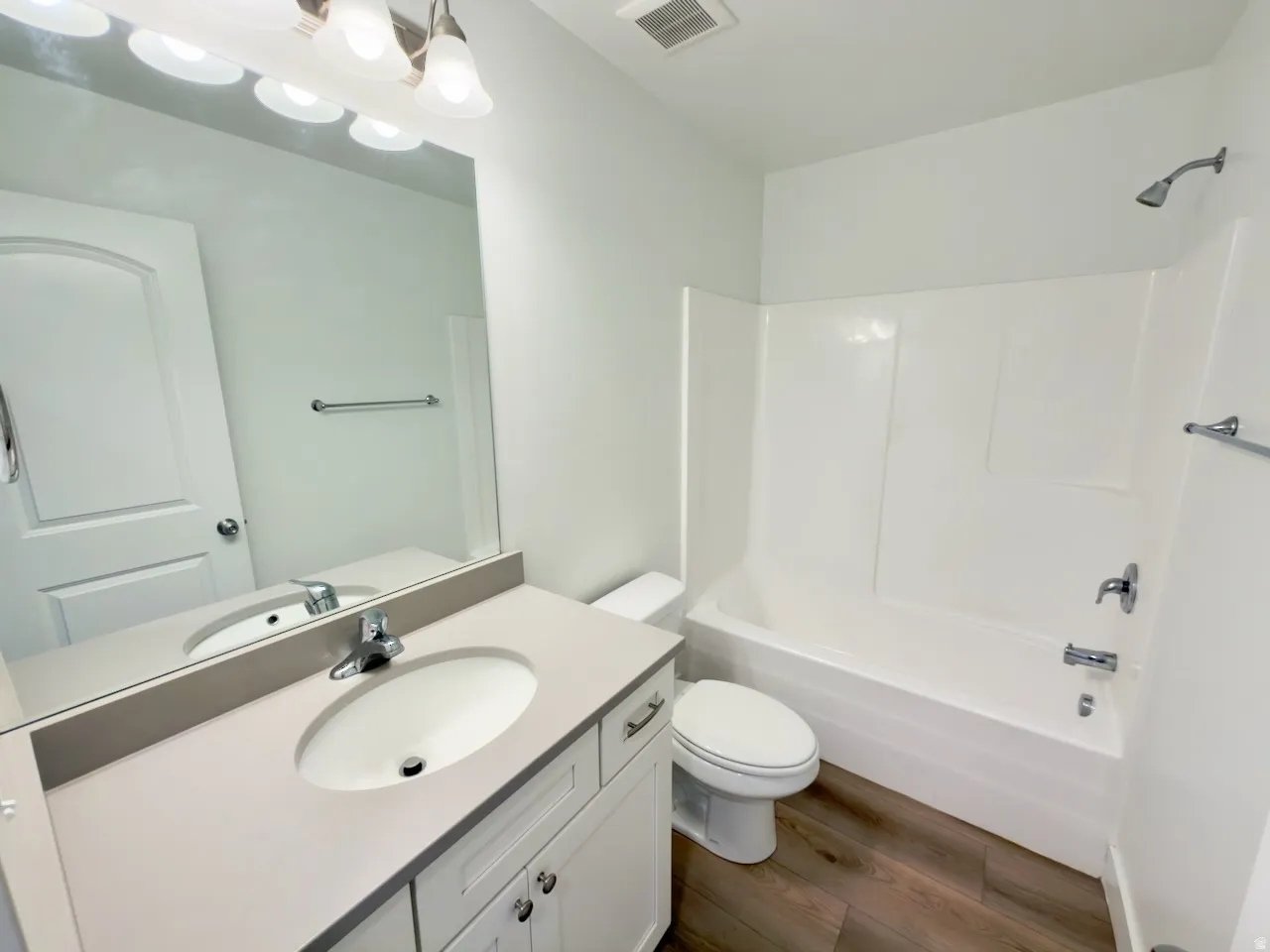 Bathroom featuring a neutral vanity with an integrated sink, polished chrome faucet, a large mirror, and a coordinating light fixture