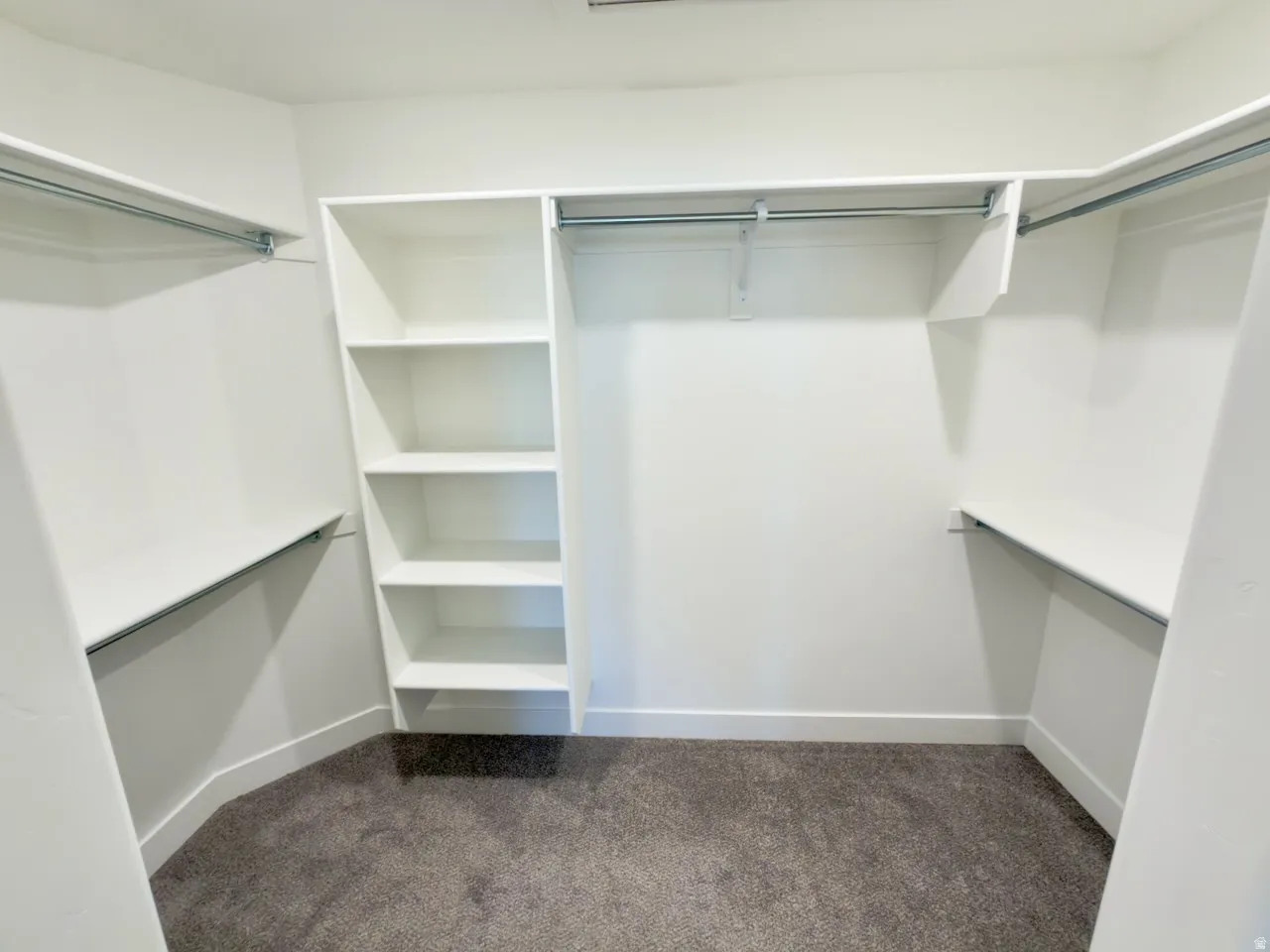 Spacious walk-in closet featuring white built-in shelving, multiple hanging rods, and plush gray carpeting