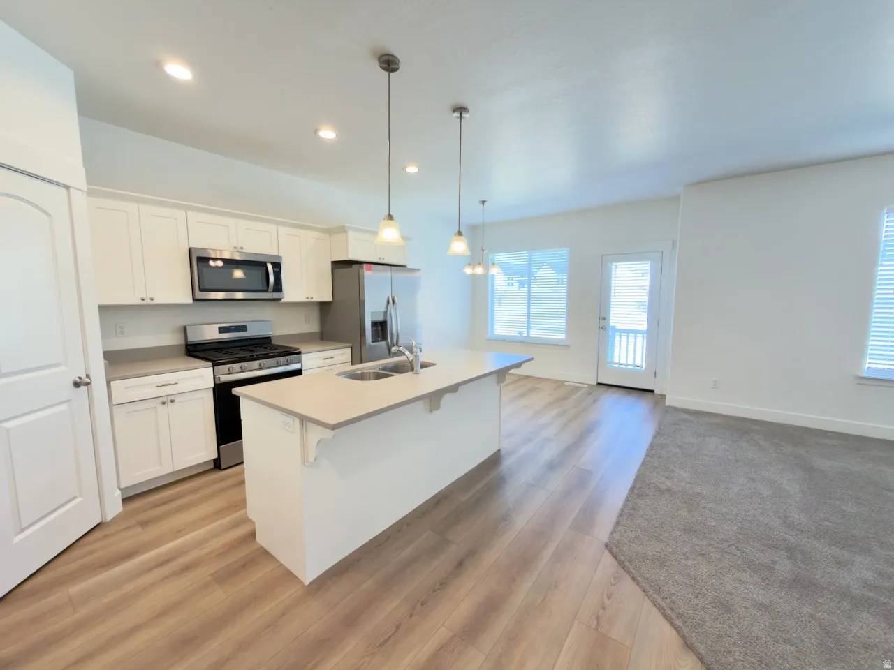 Bright kitchen featuring white cabinetry, stainless steel appliances, and a central island with integrated sink