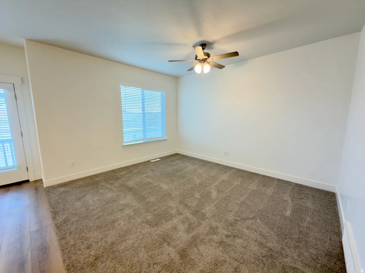 Carpeted interior space featuring a ceiling fan with integrated lighting, a large window with horizontal blinds, and a white door with glass panels