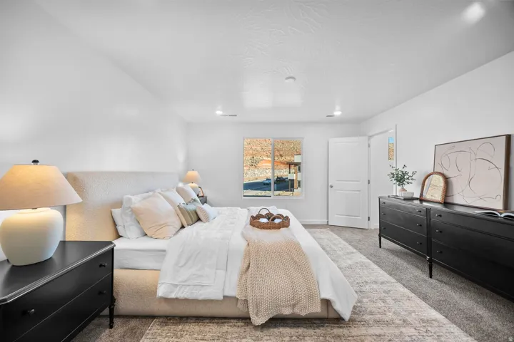 Spacious bedroom with a large window, recessed lighting, and soft gray carpeting