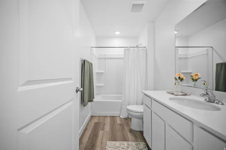 Bathroom featuring a single vanity with a white countertop and undermount sink, wood-finish flooring, and a white tub with shower