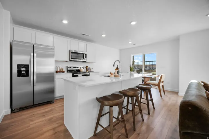 Modern kitchen featuring white cabinetry, stainless steel appliances, a center island with countertop seating, wood-finish flooring, and recessed lighting