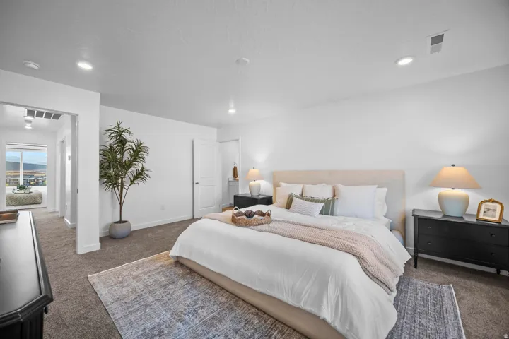 Carpeted bedroom featuring white walls, recessed lighting, and a white door leading to an adjacent area with a window
