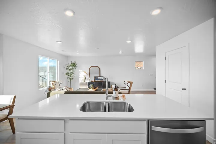 Kitchen island featuring a dual-basin stainless steel sink, a modern faucet, white cabinetry, and a built-in stainless steel dishwasher