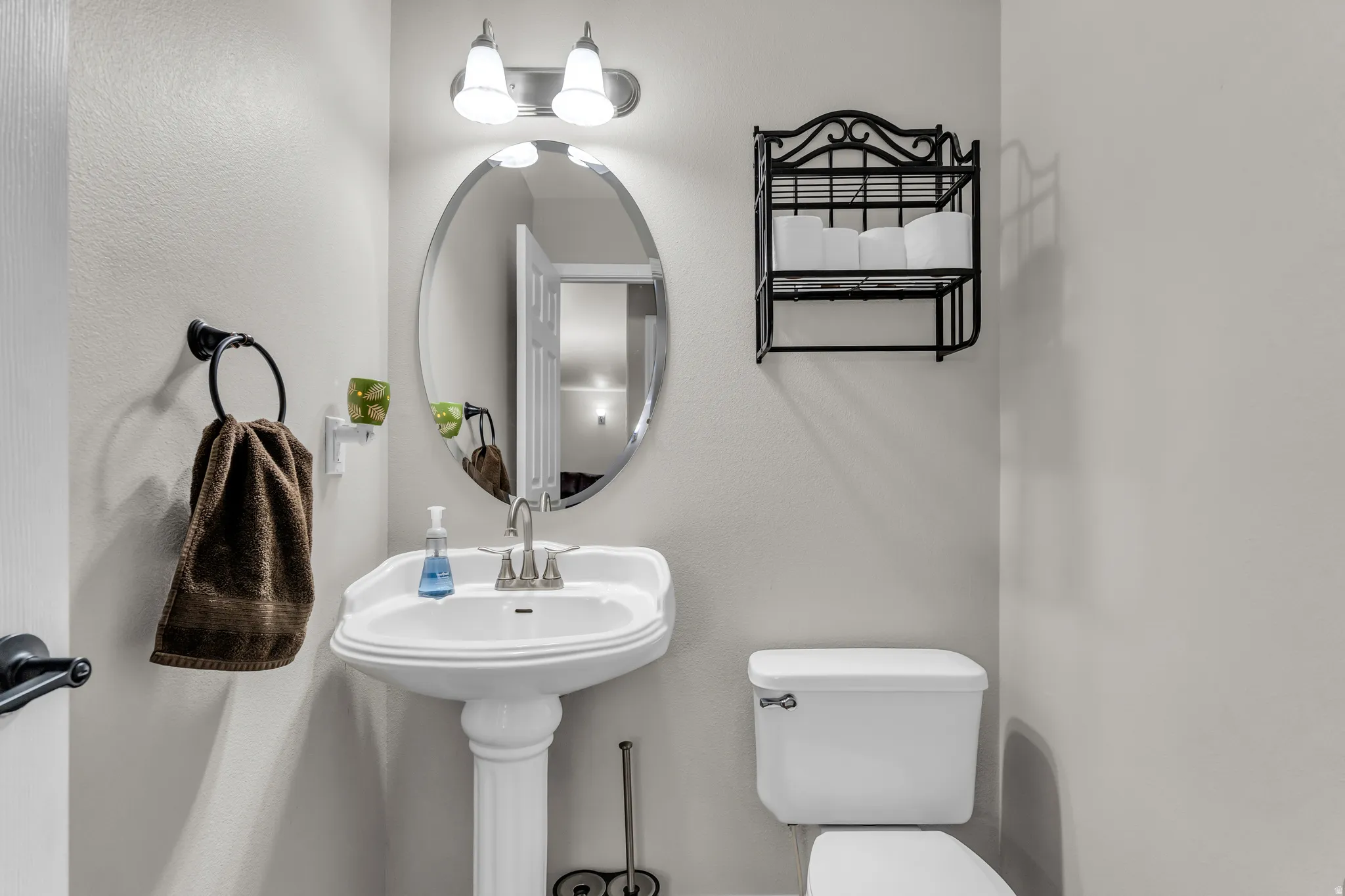 Pedestal sink with a polished chrome faucet, an oval wall mirror, and a two-light vanity fixture
