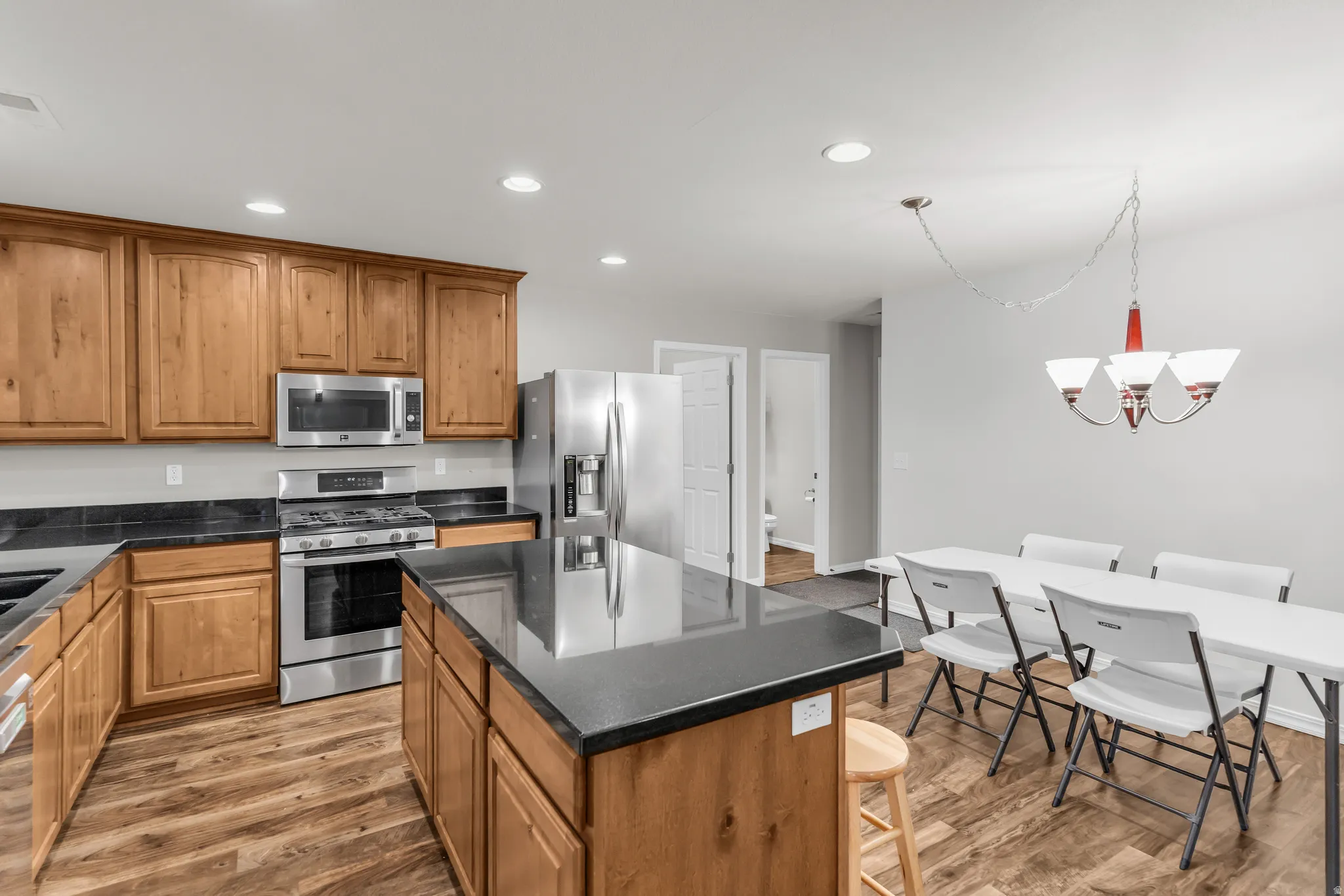 Kitchen featuring wood-finish flooring, stainless steel appliances, dark countertops, recessed lighting, and a central island