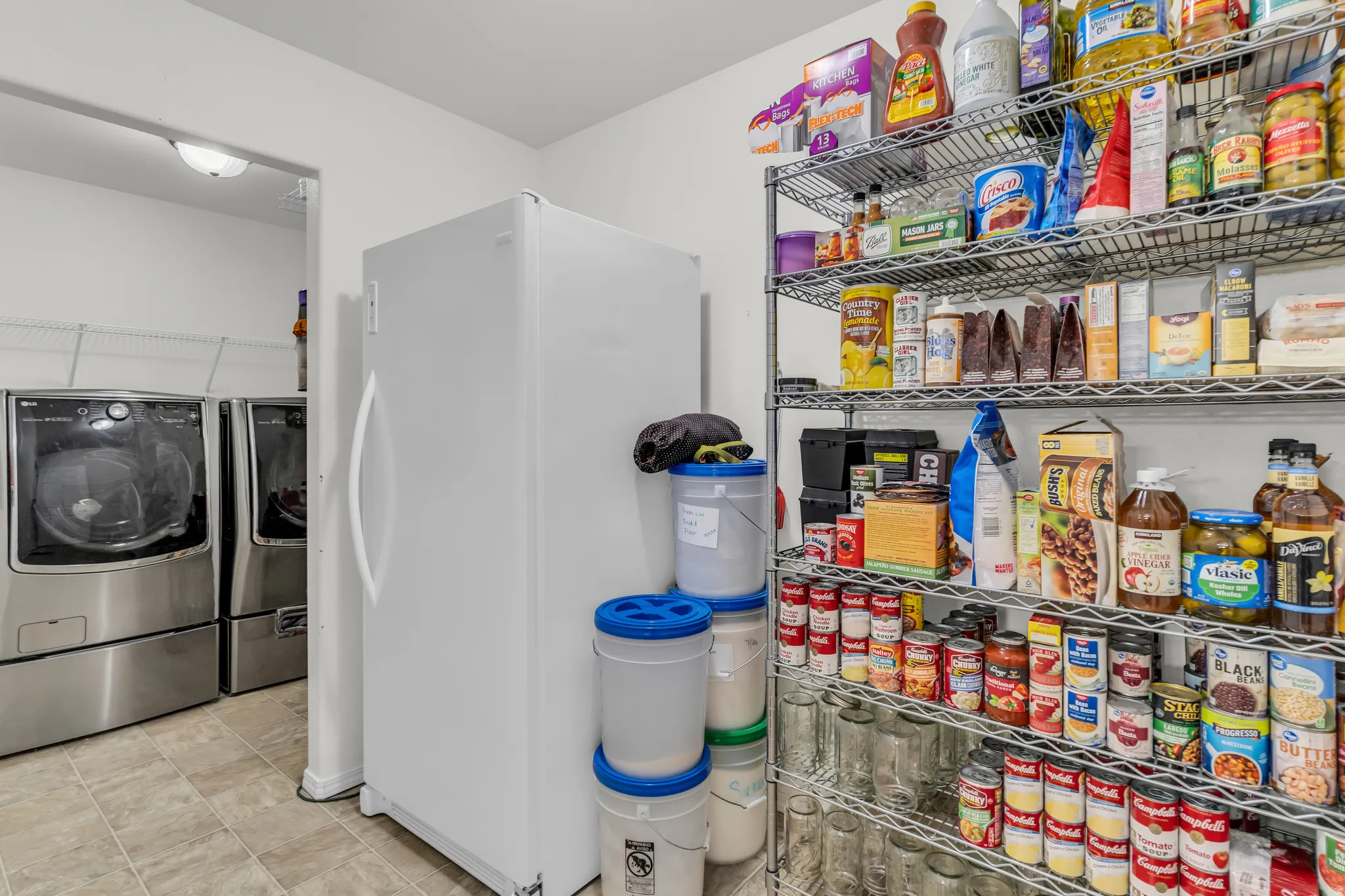 Integrated pantry and utility area featuring wire shelving, a full-size refrigerator, and tile flooring