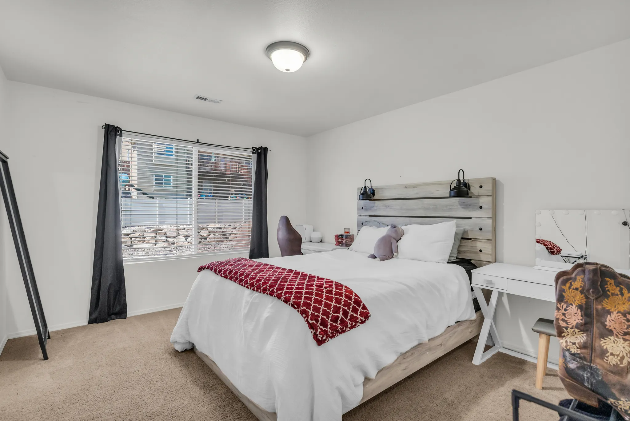 Carpeted bedroom featuring a large window with blinds, white walls, and a ceiling-mounted light fixture