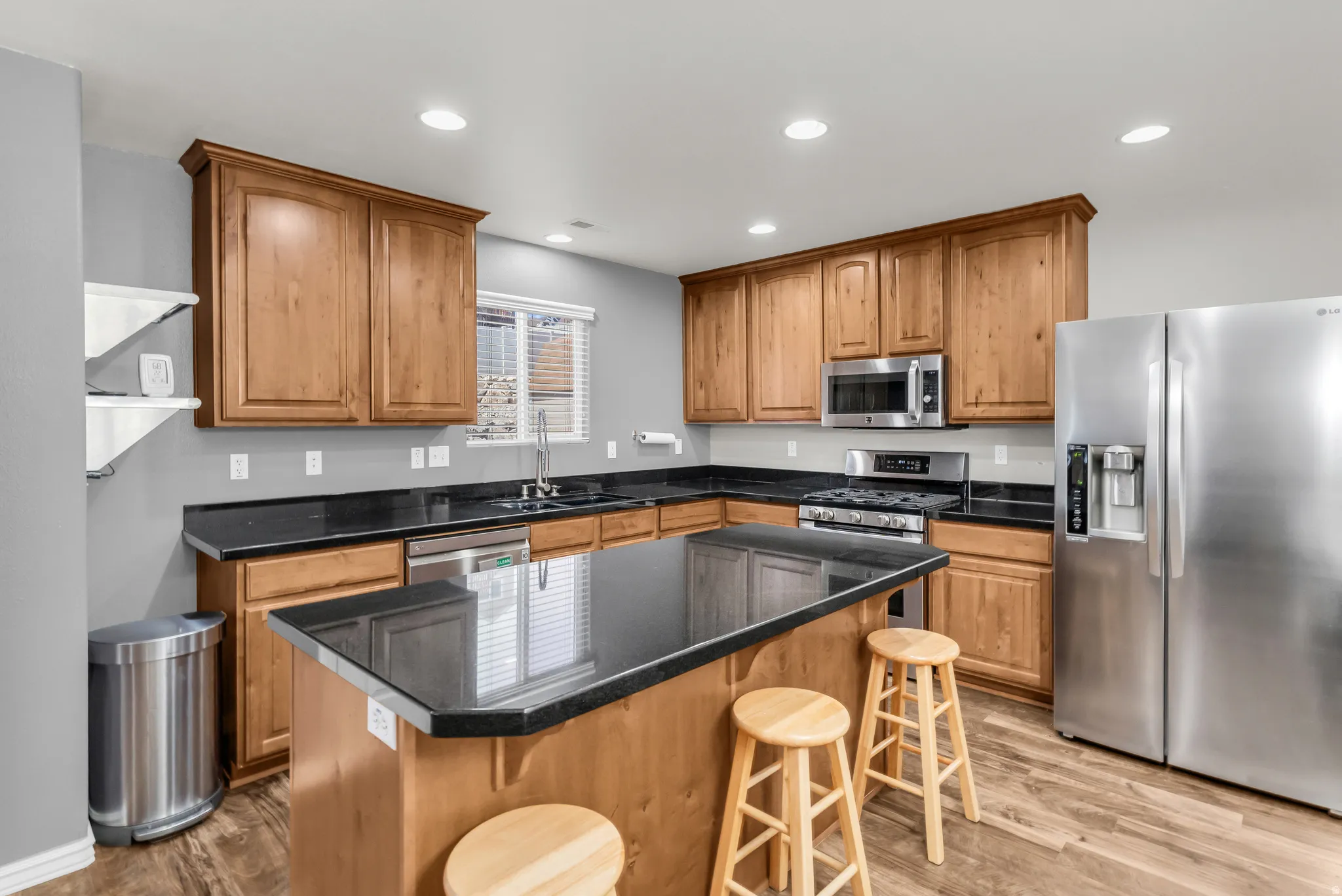 Kitchen featuring wood cabinetry, dark countertops, stainless steel appliances, and wood-finish flooring