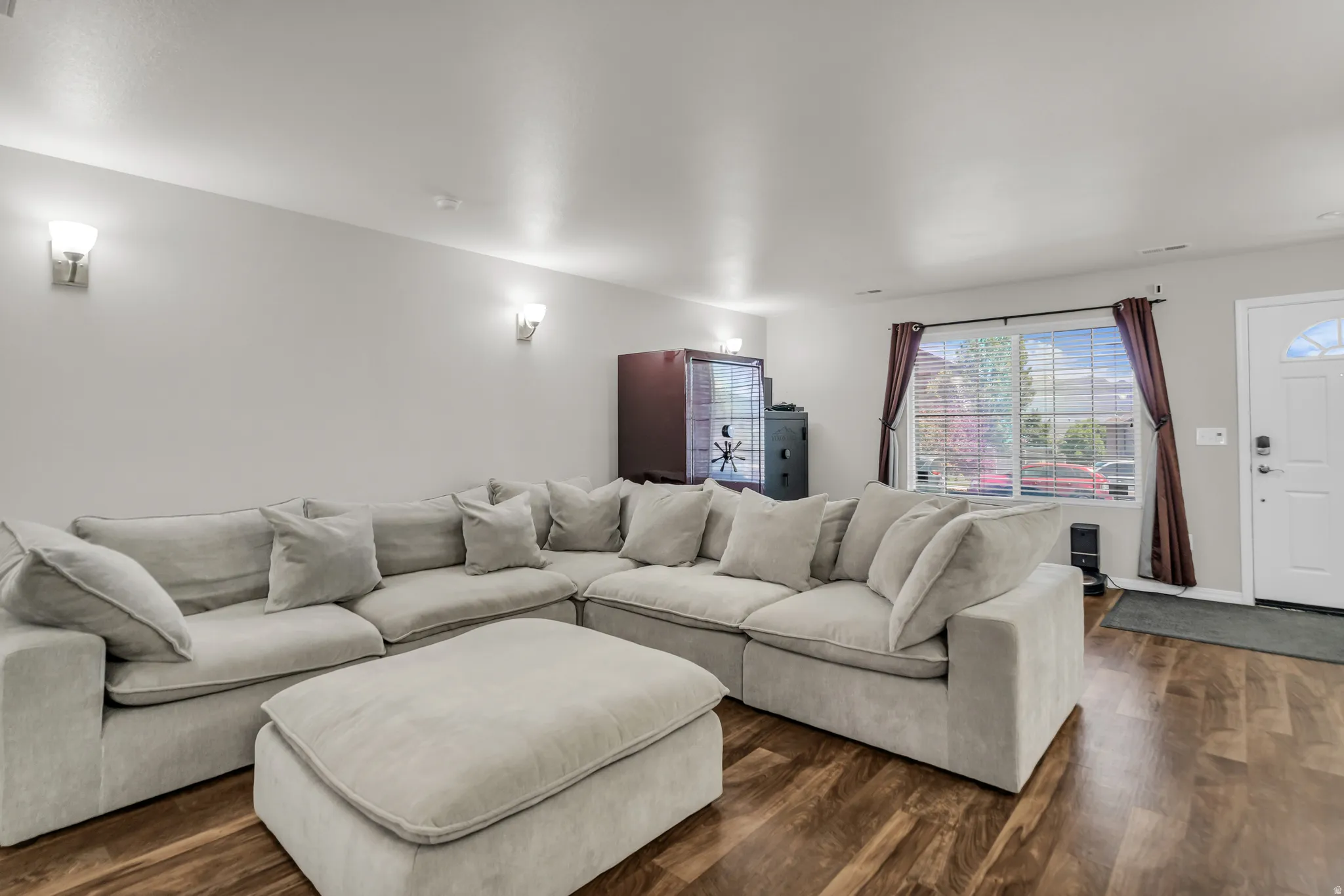 Spacious living area featuring wood-finish flooring, light grey wall paint, and wall-mounted sconces