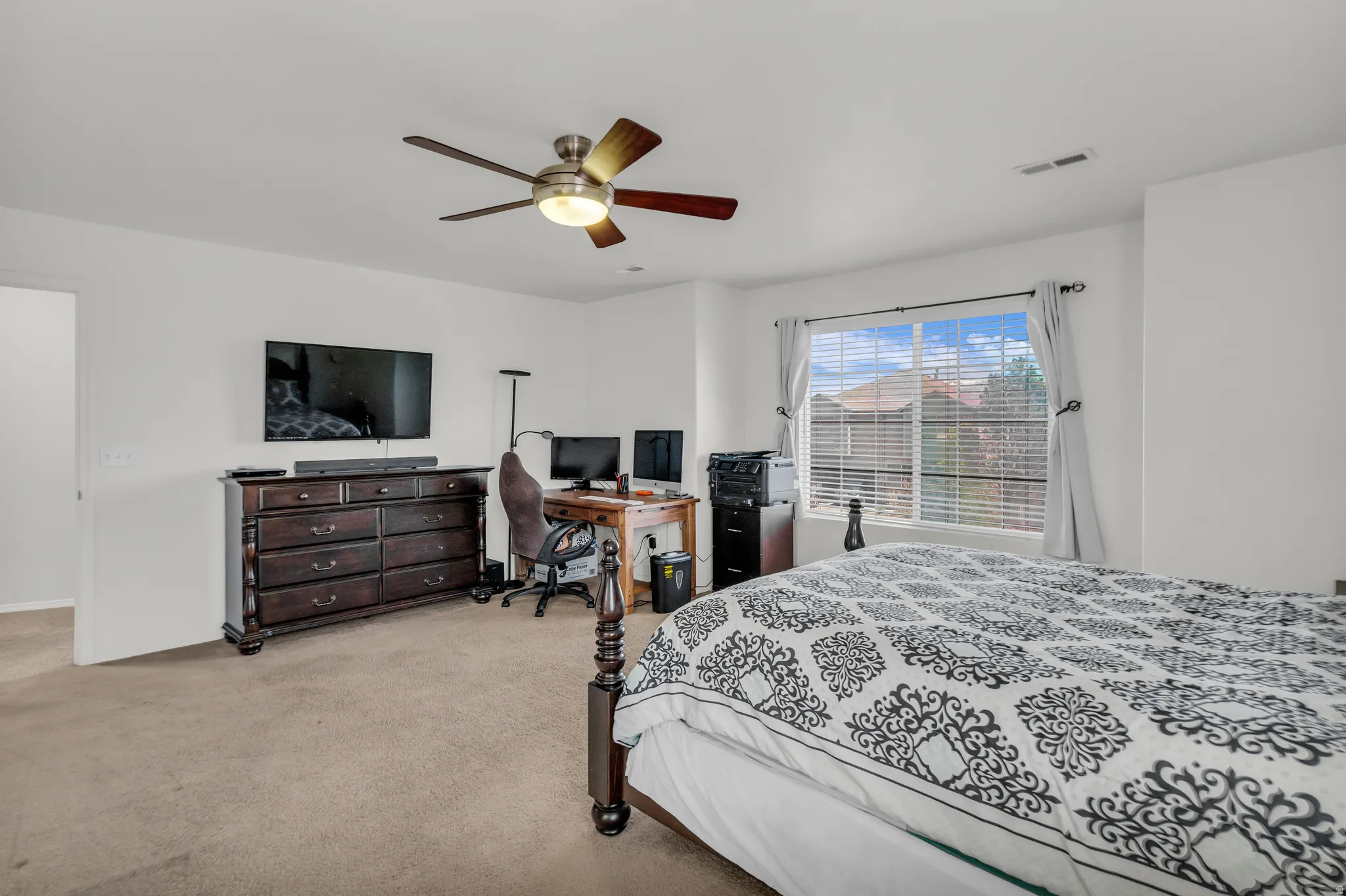 Spacious room featuring neutral carpet flooring, a large window with horizontal blinds, and a ceiling fan with integrated lighting