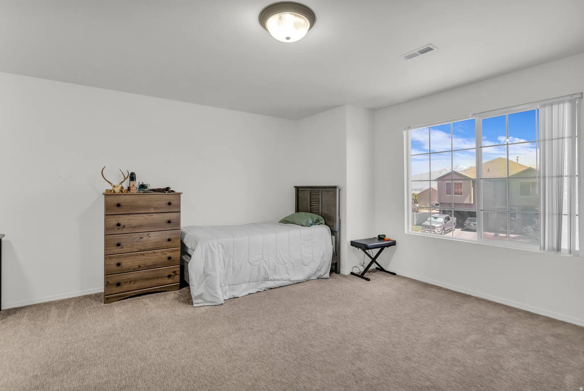 Spacious room featuring neutral carpeting, white wall finishes, a large window with vertical blinds, and a ceiling-mounted light fixture