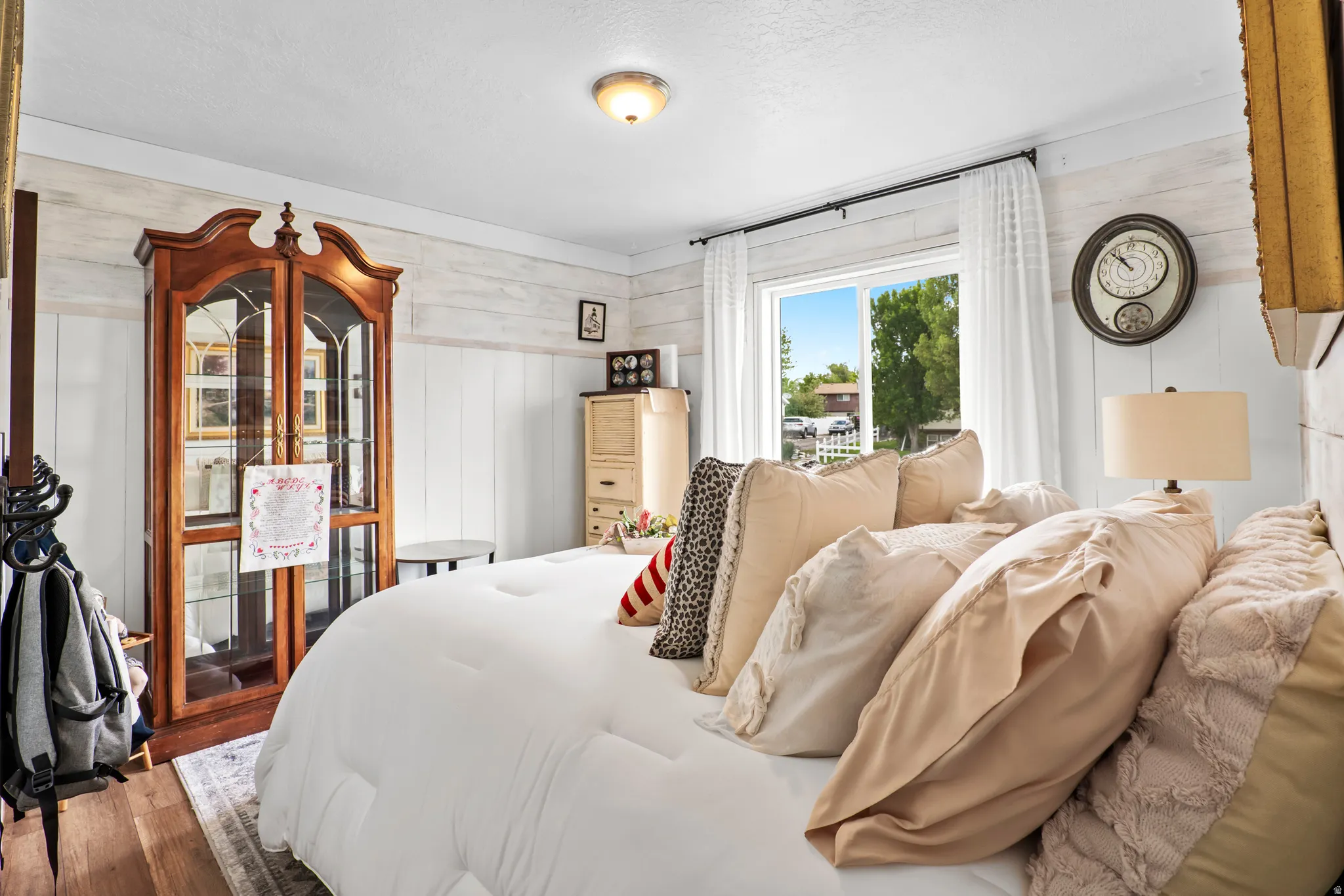 Bedroom featuring wood-finish flooring, a double window with white curtains, white shiplap walls, and a ceiling-mounted light fixture