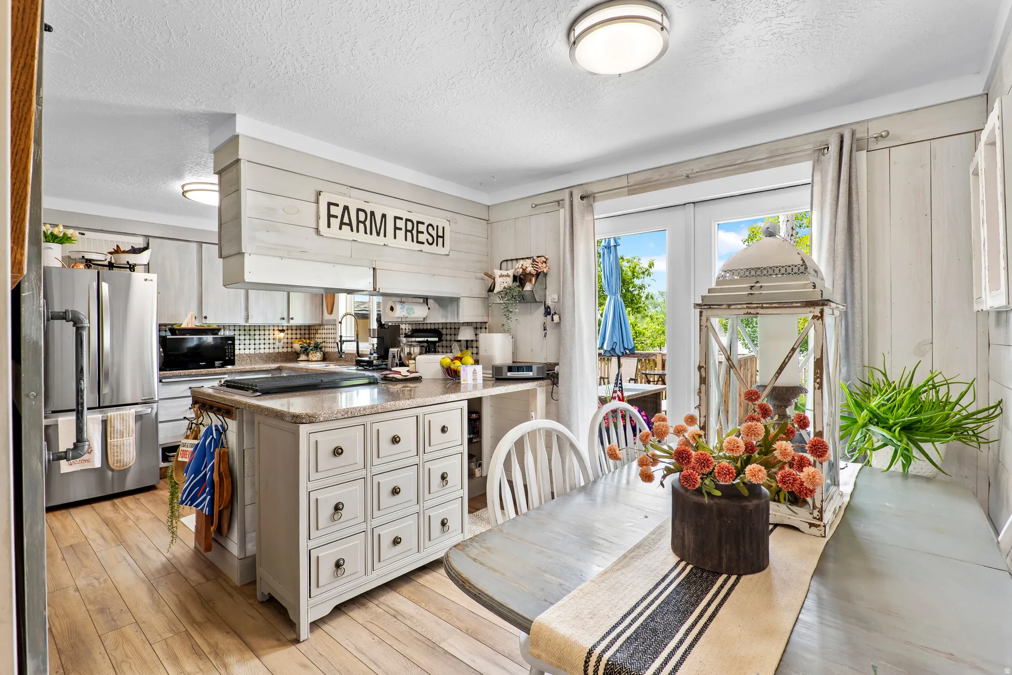 Spacious kitchen featuring a central island with integrated storage, wood-finish flooring, stainless steel appliances, and French doors opening to an outdoor area