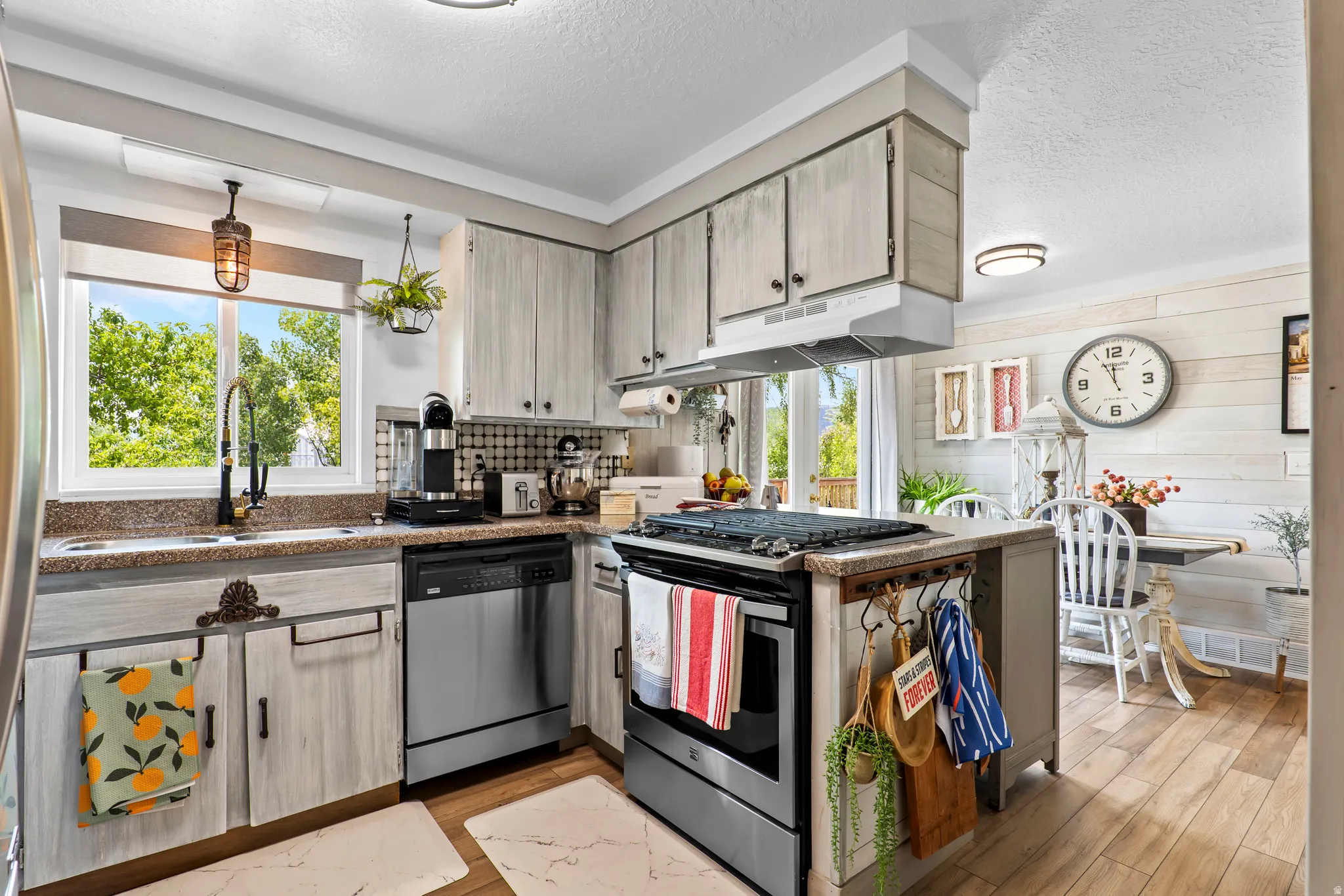 Kitchen featuring wood-finish flooring, light-toned cabinetry, a stainless steel dishwasher, and a stone-finish countertop