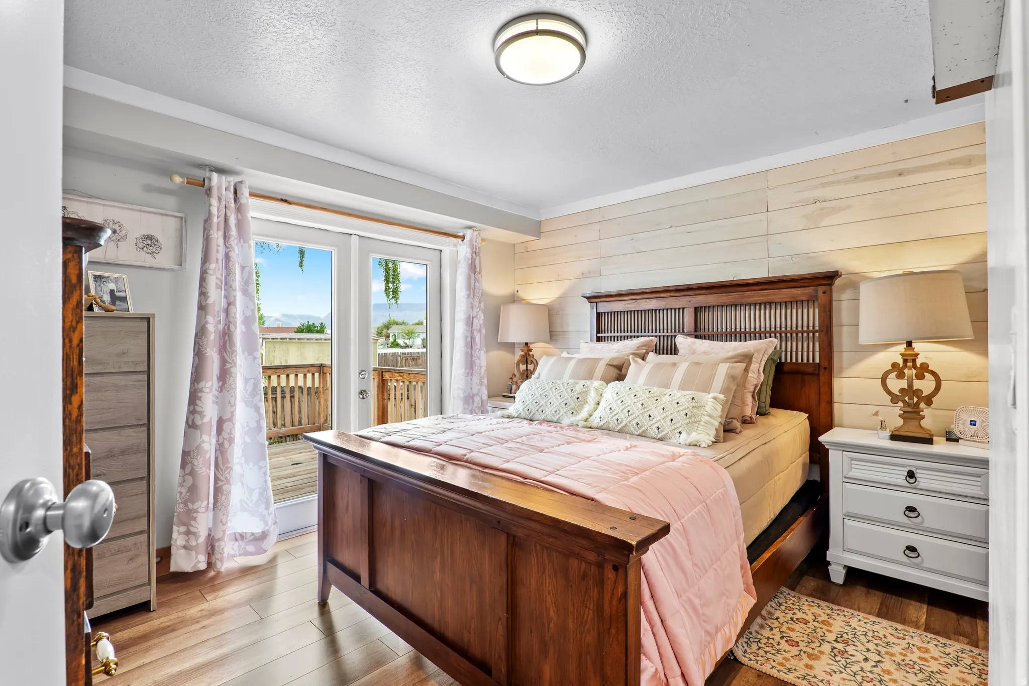 Bedroom featuring wood-finish flooring, a shiplap accent wall, white trim, and a glass-paneled double door opening to a deck