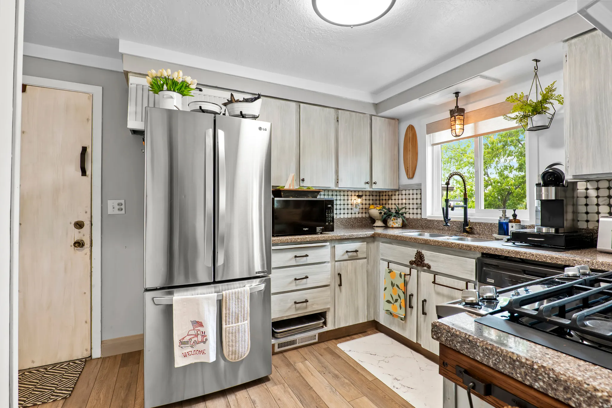 Kitchen featuring wood-finish flooring, light-toned cabinetry with dark hardware, a patterned backsplash, and a window above the sink