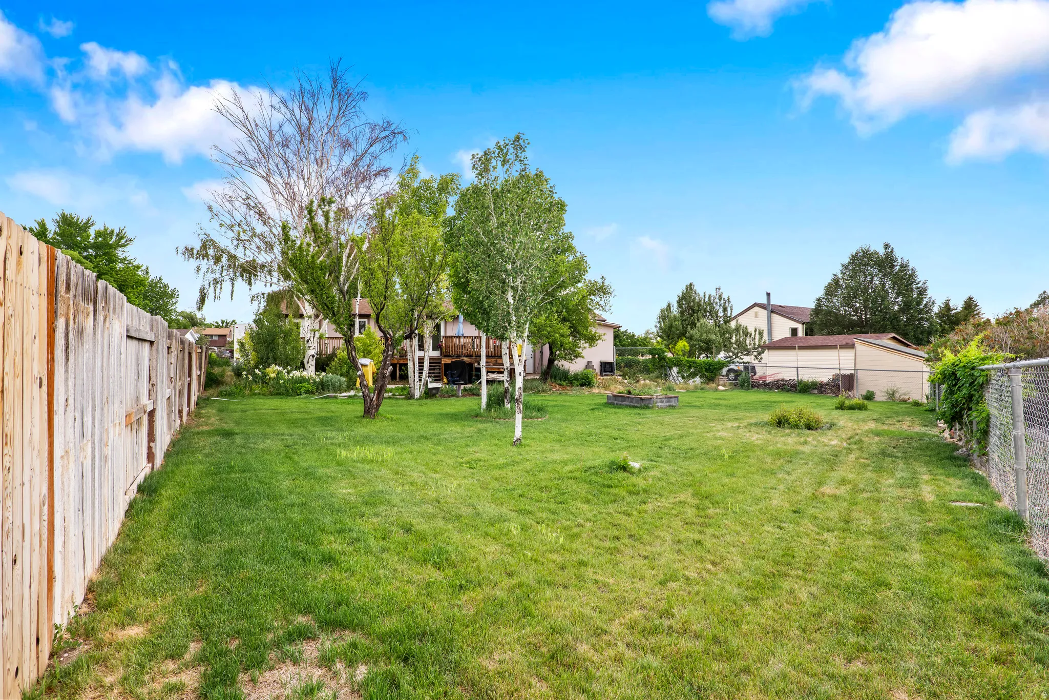 Expansive green lawn with a wooden privacy fence, mature trees, and a raised garden bed