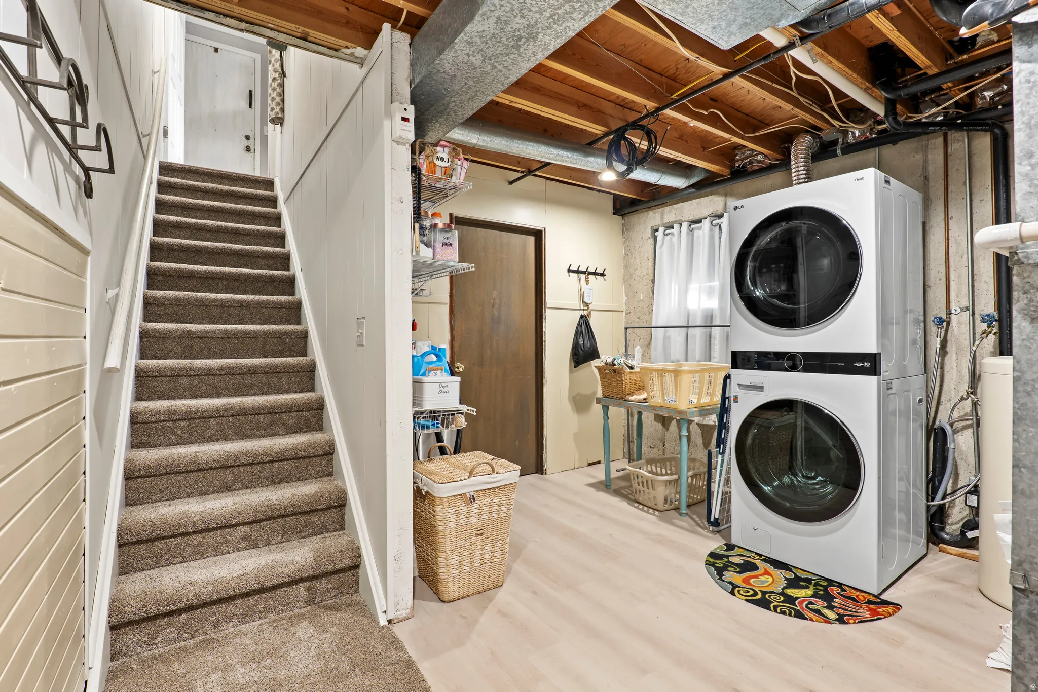 Utility area featuring light wood-finish flooring, exposed ceiling joists, and concrete walls