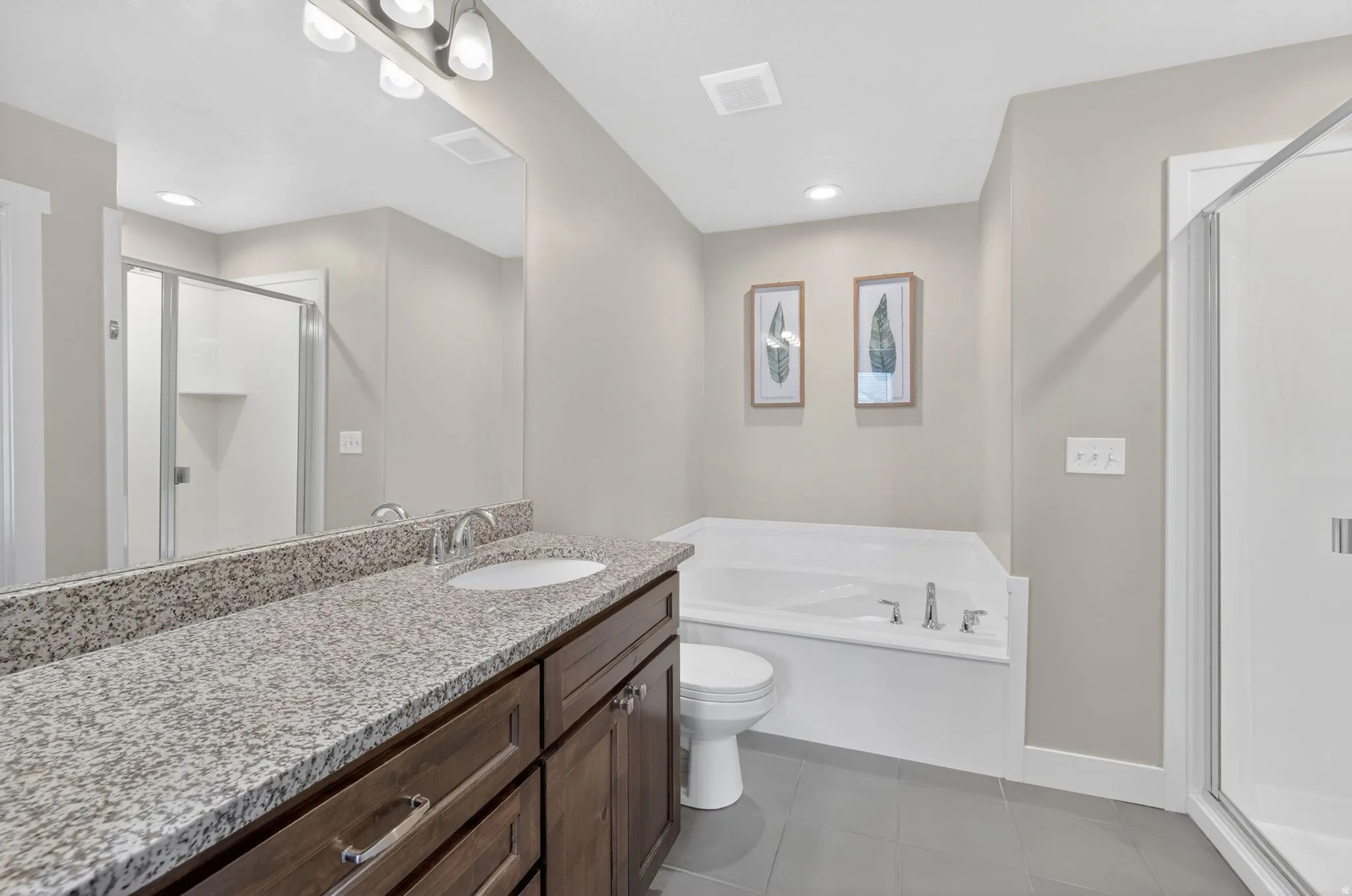Bathroom featuring a spacious double vanity with a speckled countertop, a built-in soaking tub, and a separate glass-enclosed shower