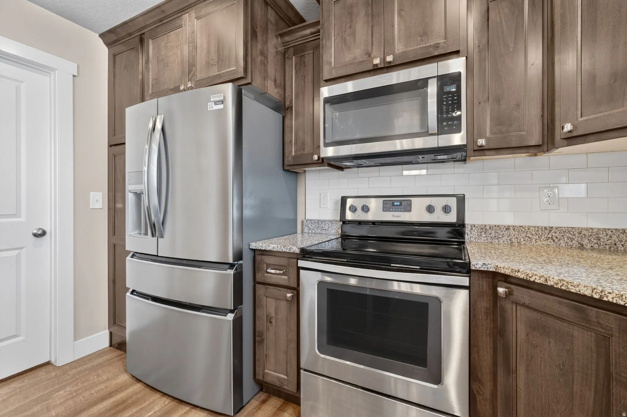Kitchen featuring stainless steel appliances, wood-finish flooring, wood cabinetry, light-toned countertops, and a white subway tile backsplash