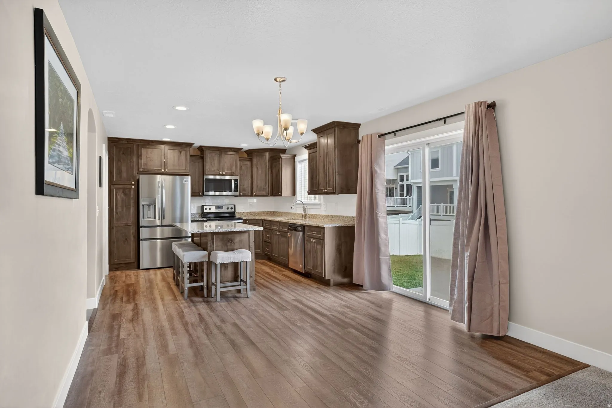 Open-concept kitchen and dining area featuring wood-finish flooring, dark wood cabinetry, stainless steel appliances, and a central island with countertop seating