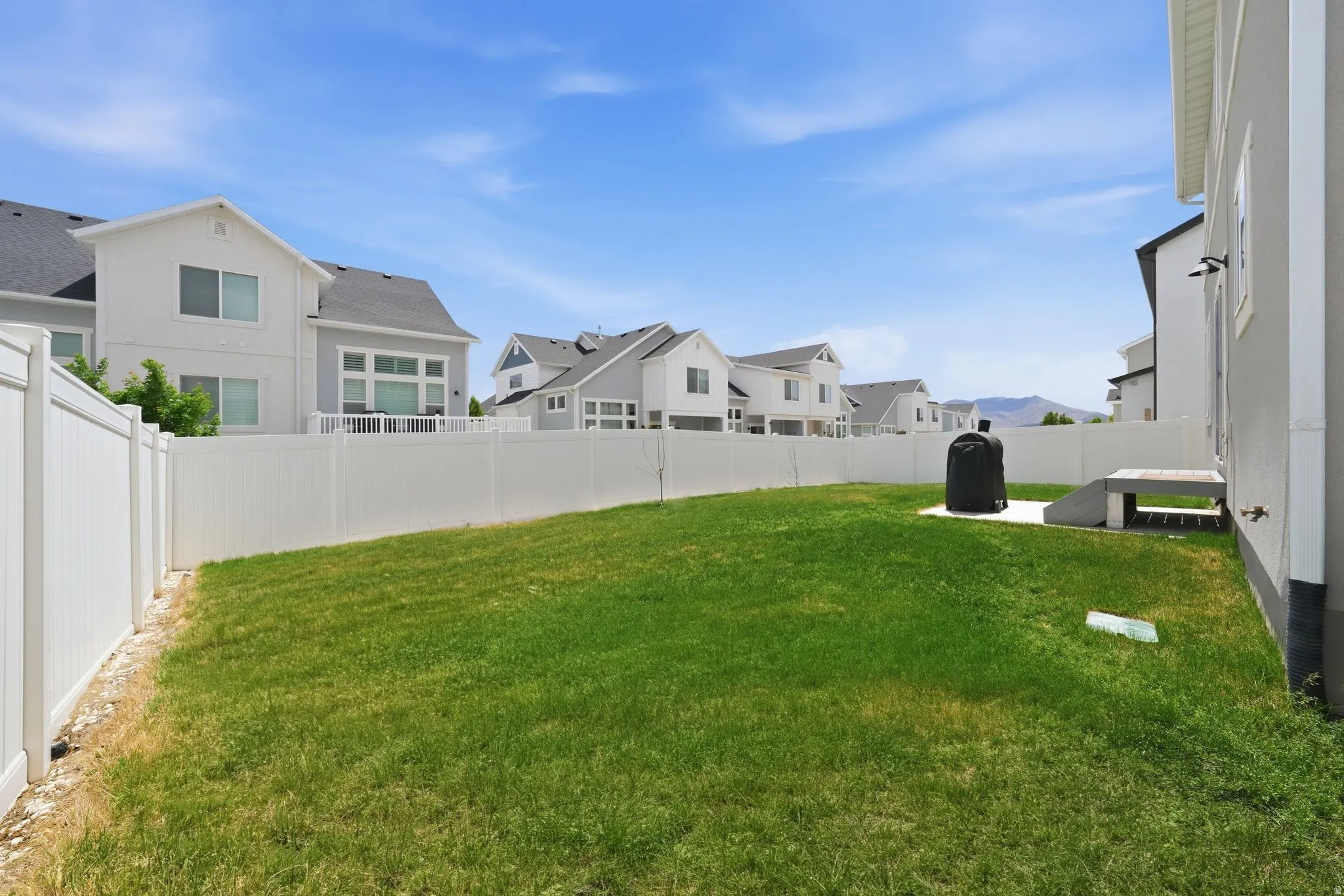 Expansive backyard featuring a lush lawn, privacy fencing, and a concrete patio