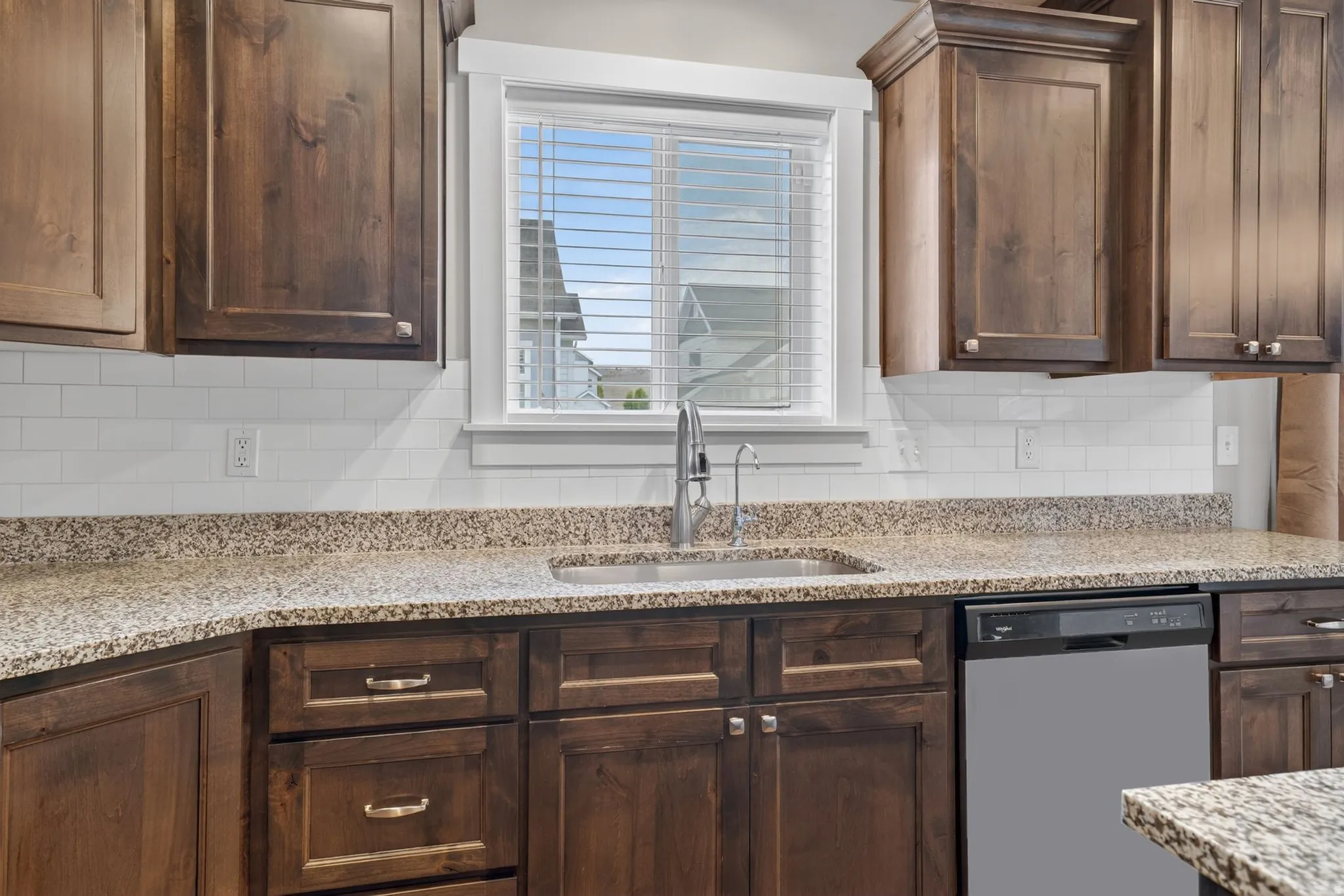 Kitchen featuring wood-finish cabinetry, speckled countertops, a stainless steel sink with a gooseneck faucet, a white subway tile backsplash, and a black dishwasher