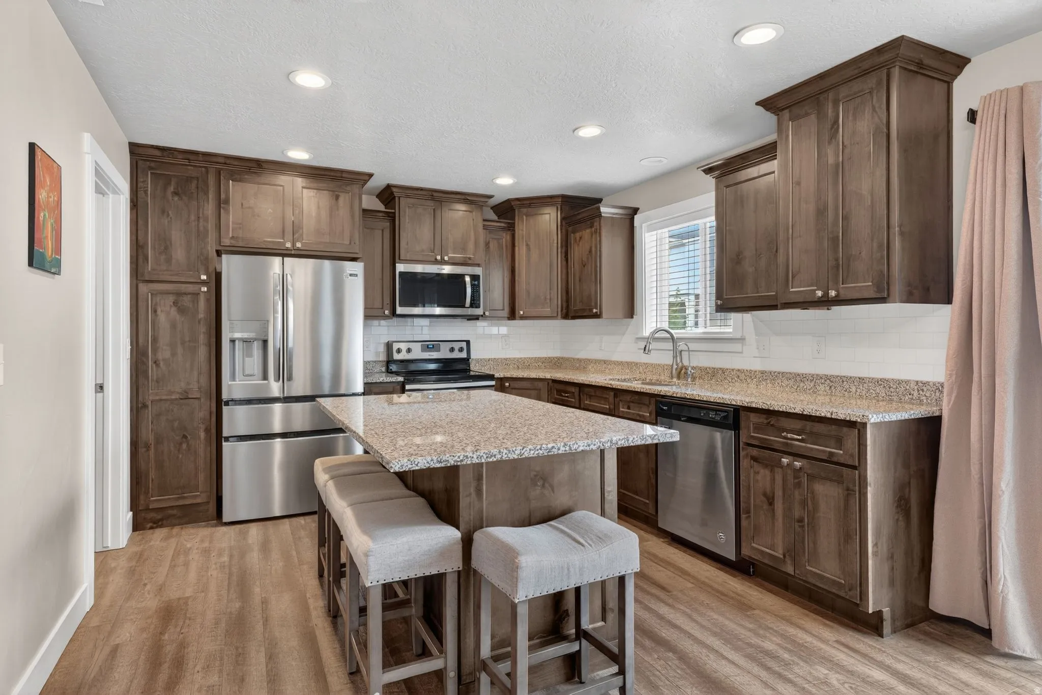 Kitchen featuring a central island with countertop seating, wood-finish flooring, stainless steel appliances, extensive cabinetry, and granite countertops