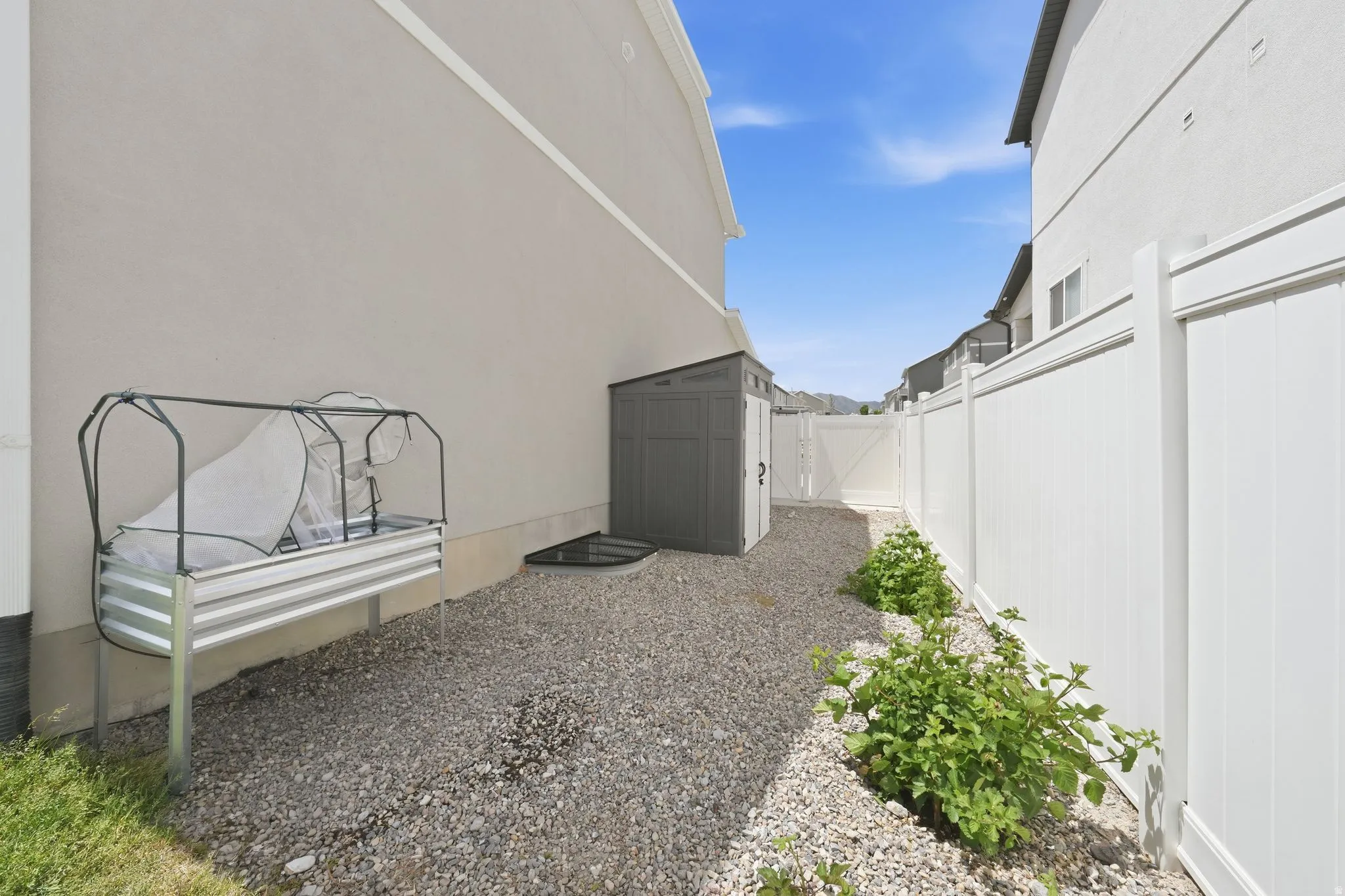 Gravel pathway with a white privacy fence, garden beds, and an exterior storage shed