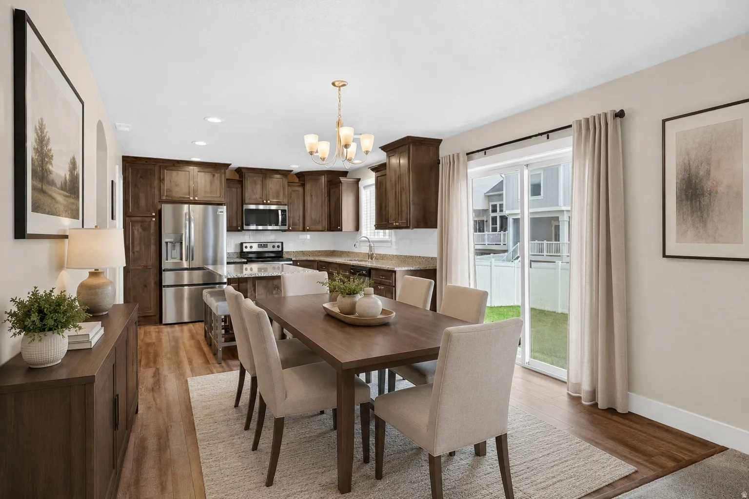 Open-concept living space featuring wood-finish flooring, dark wood cabinetry, stainless steel appliances, granite countertops, and a sliding glass door to the backyard