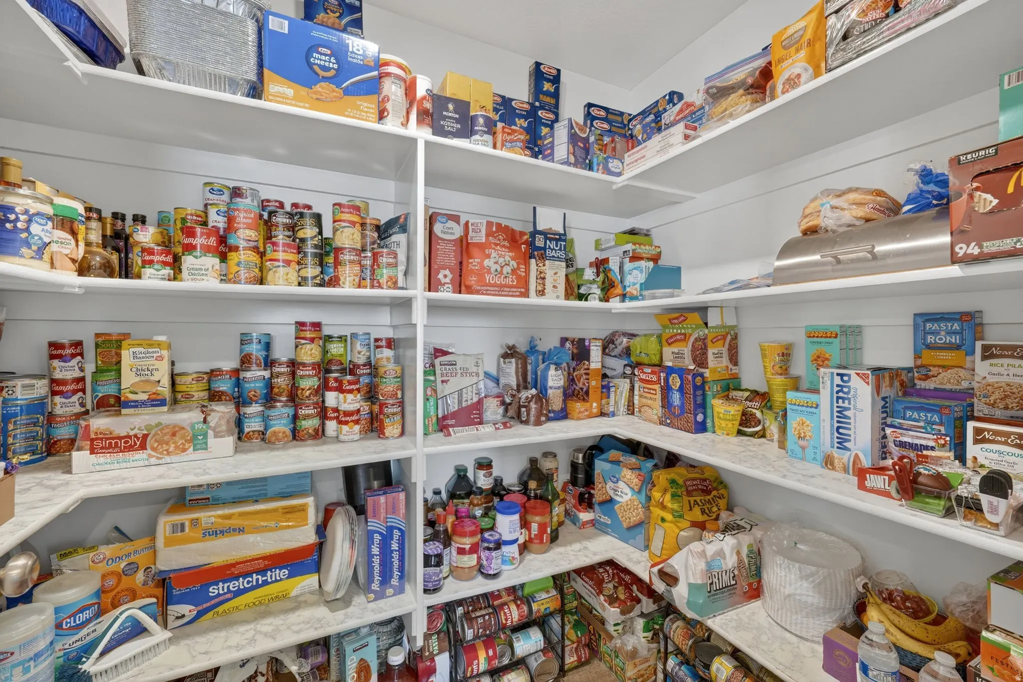 Walk-in pantry featuring extensive built-in shelving, white flat-panel cabinetry, and L-shaped countertop surfaces
