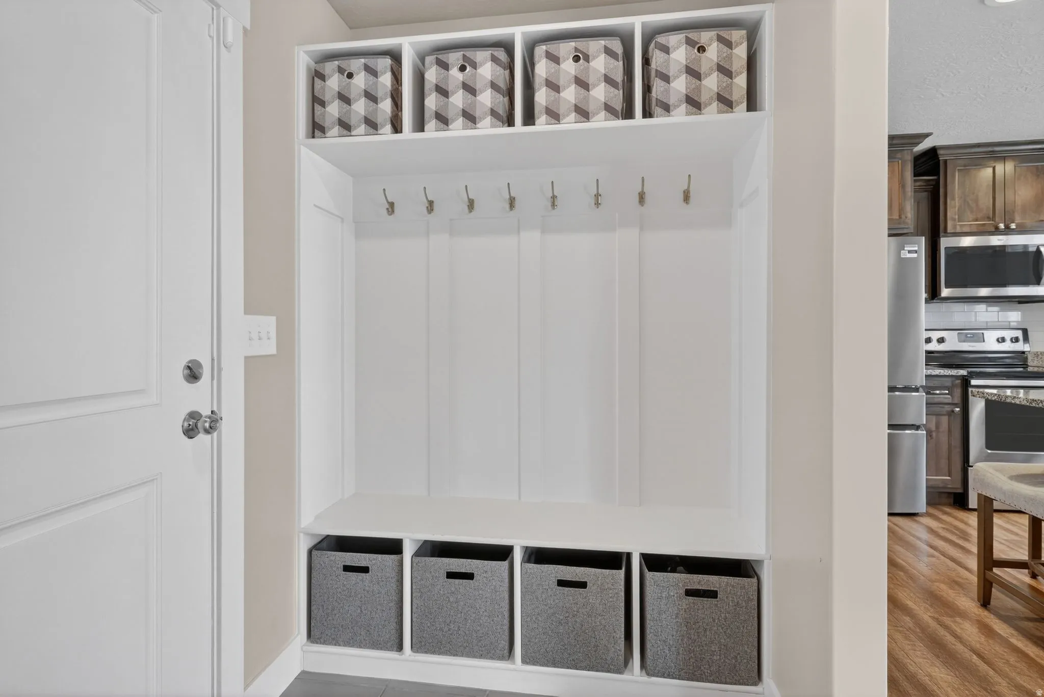 Built-in mudroom storage featuring white paneling, upper shelving, multiple coat hooks, and lower cubbies