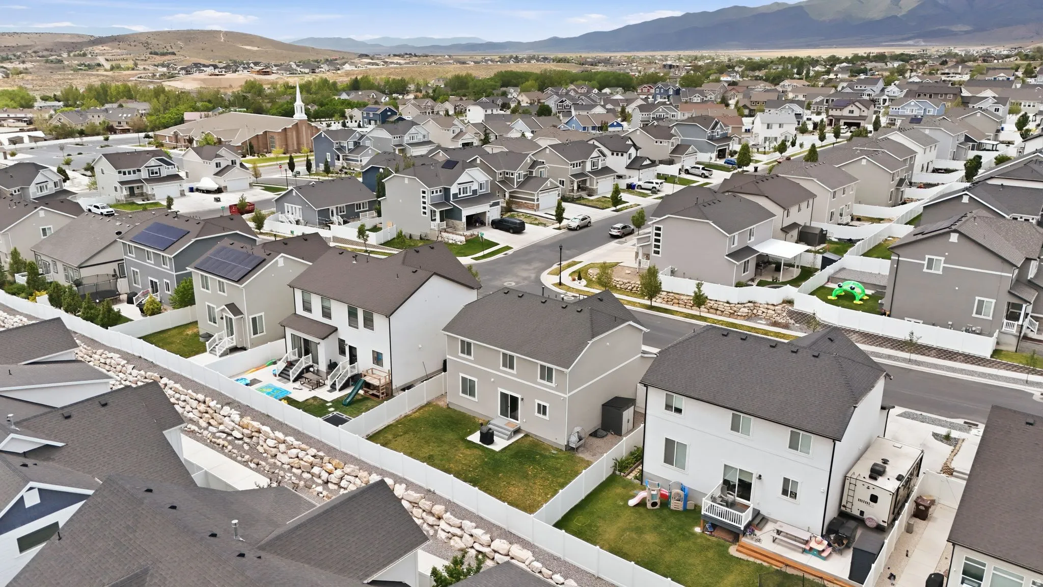 Residential development featuring multiple properties with dark shingle roofs, vinyl siding, and white perimeter fencing