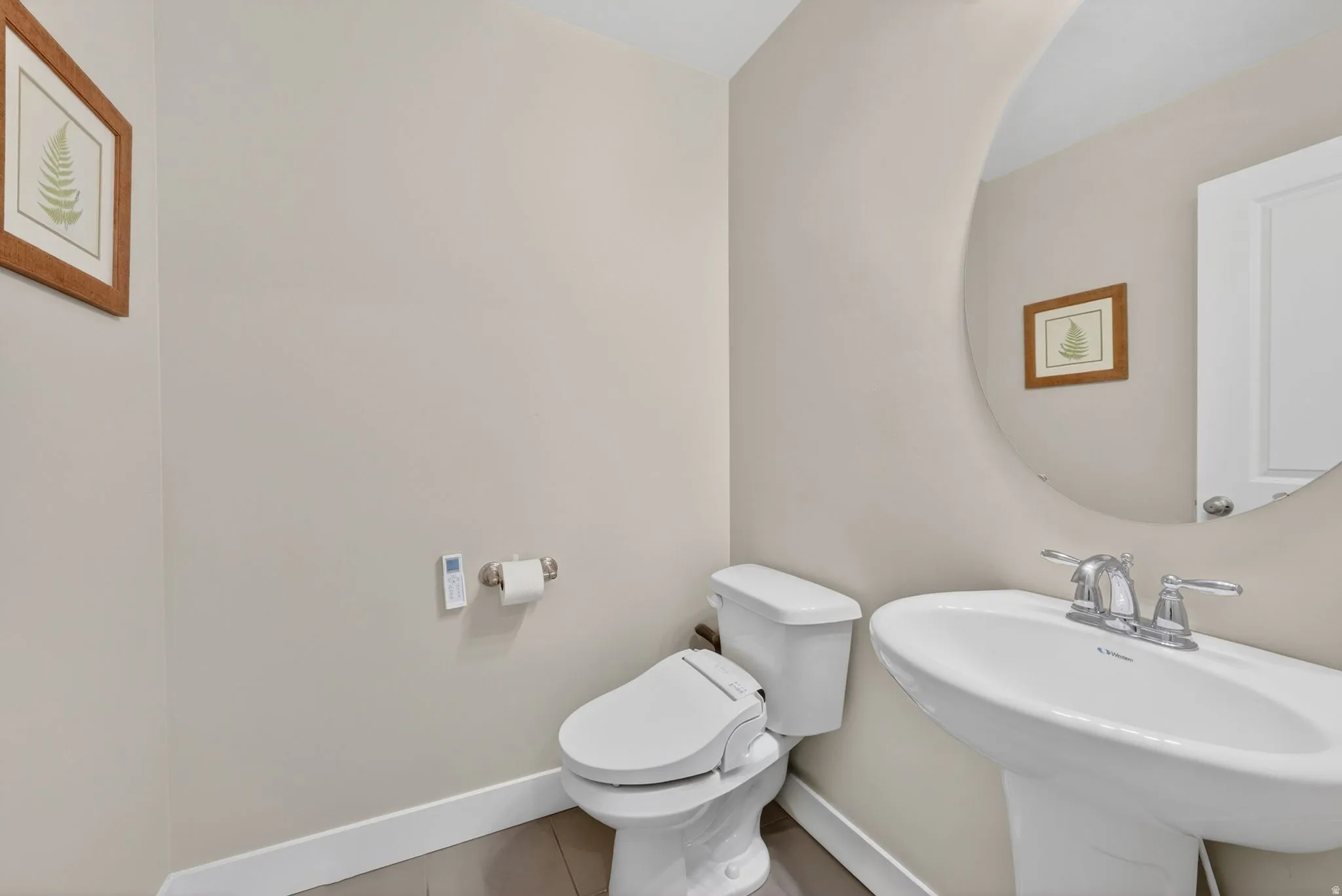 Pedestal sink with chrome faucet, circular mirror, and wood-finish flooring