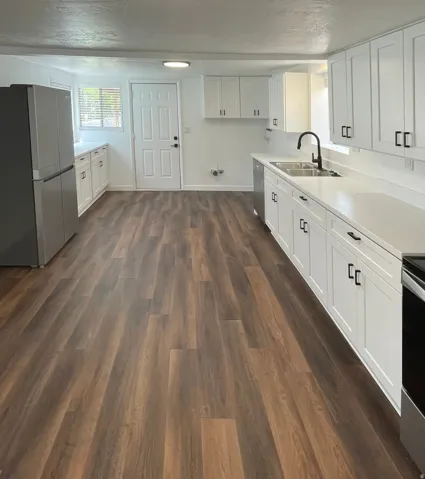 Kitchen featuring wood-finish flooring, white cabinetry with dark hardware, white countertops, a stainless steel sink with a dark-finish faucet, and a stainless steel refrigerator