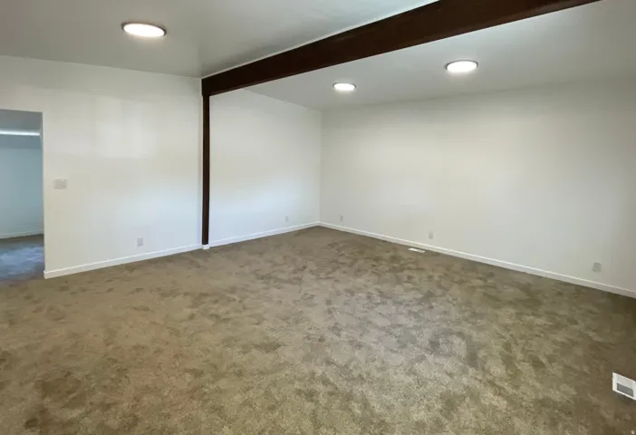 Spacious interior room featuring light beige carpeting, white walls, and a white ceiling with recessed lighting