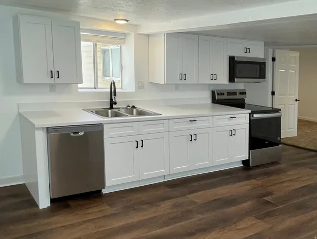 Modern kitchen featuring white shaker cabinetry, stainless steel appliances, a double basin sink with a matte black faucet, and wood-finish flooring