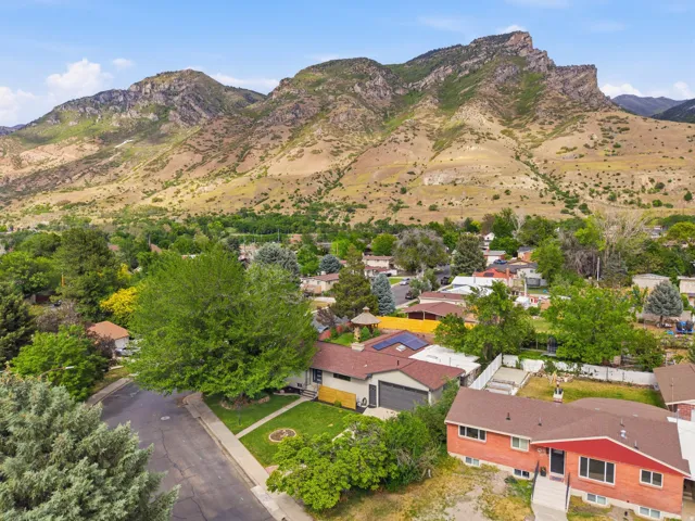Expansive mountain backdrop with a residential neighborhood featuring mature trees, a red brick exterior home with a brown roof, and a paved driveway