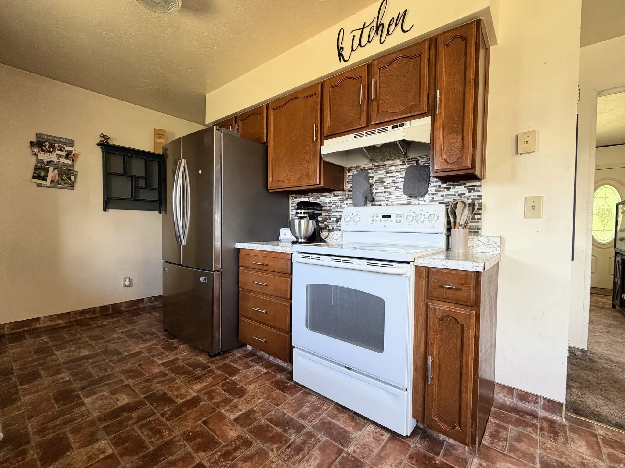 Kitchen featuring wood-finish cabinetry, a white electric range, a mosaic tile backsplash, and a stainless steel refrigerator