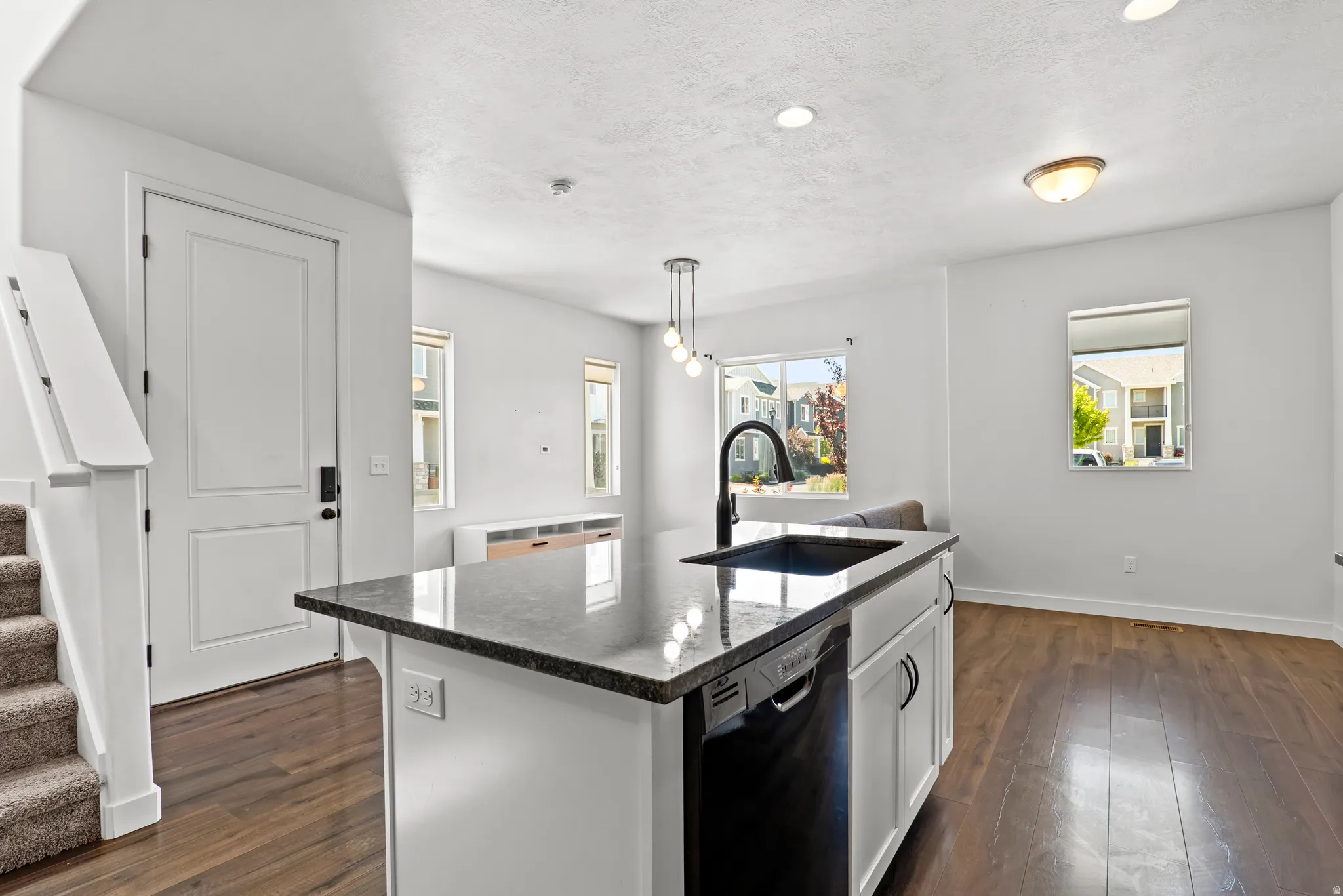 Kitchen island featuring a dark countertop, an undermount sink with a gooseneck faucet, and integrated dishwasher