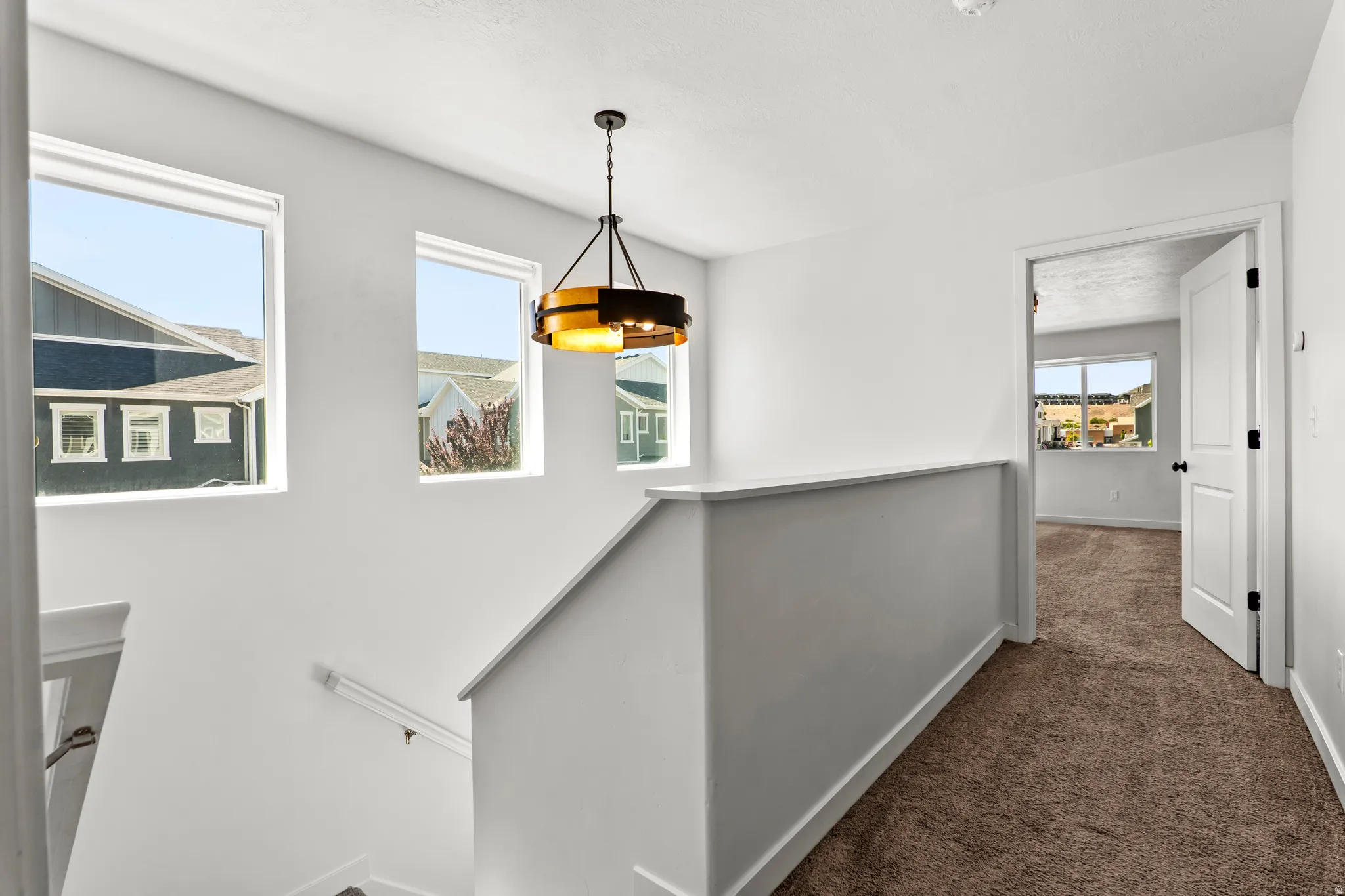 Upper-level landing featuring a contemporary chandelier, multiple windows for natural light, and plush brown carpeting extending into a room with a large window