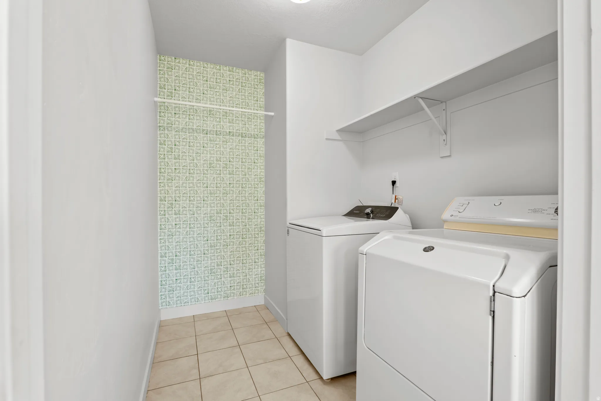 Dedicated laundry space featuring neutral tile flooring and a patterned accent wall