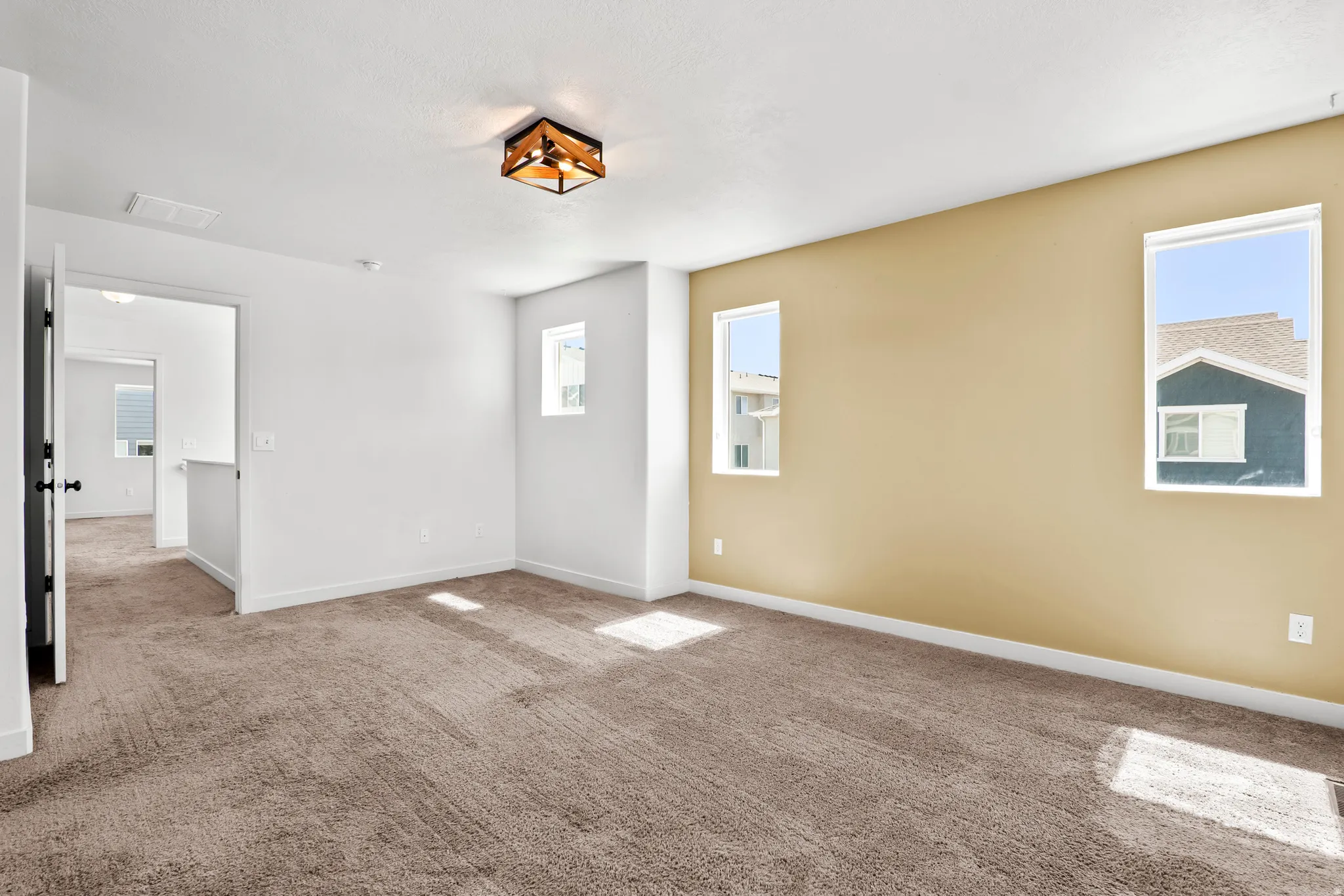 Carpeted room featuring a gold accent wall, multiple windows, and a wood-finish ceiling light fixture