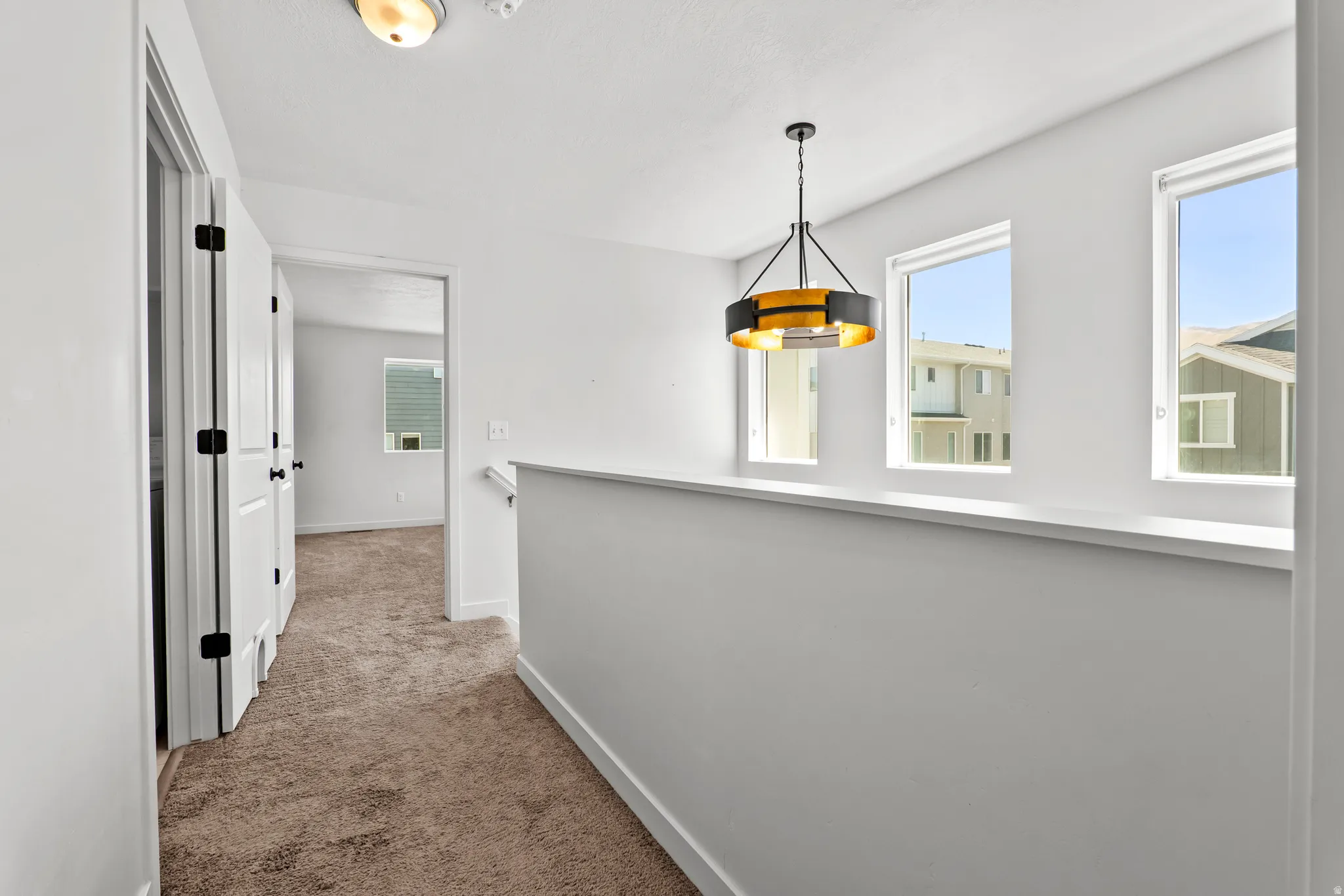 Hallway with plush brown carpeting, a contemporary drum chandelier, and a white railing