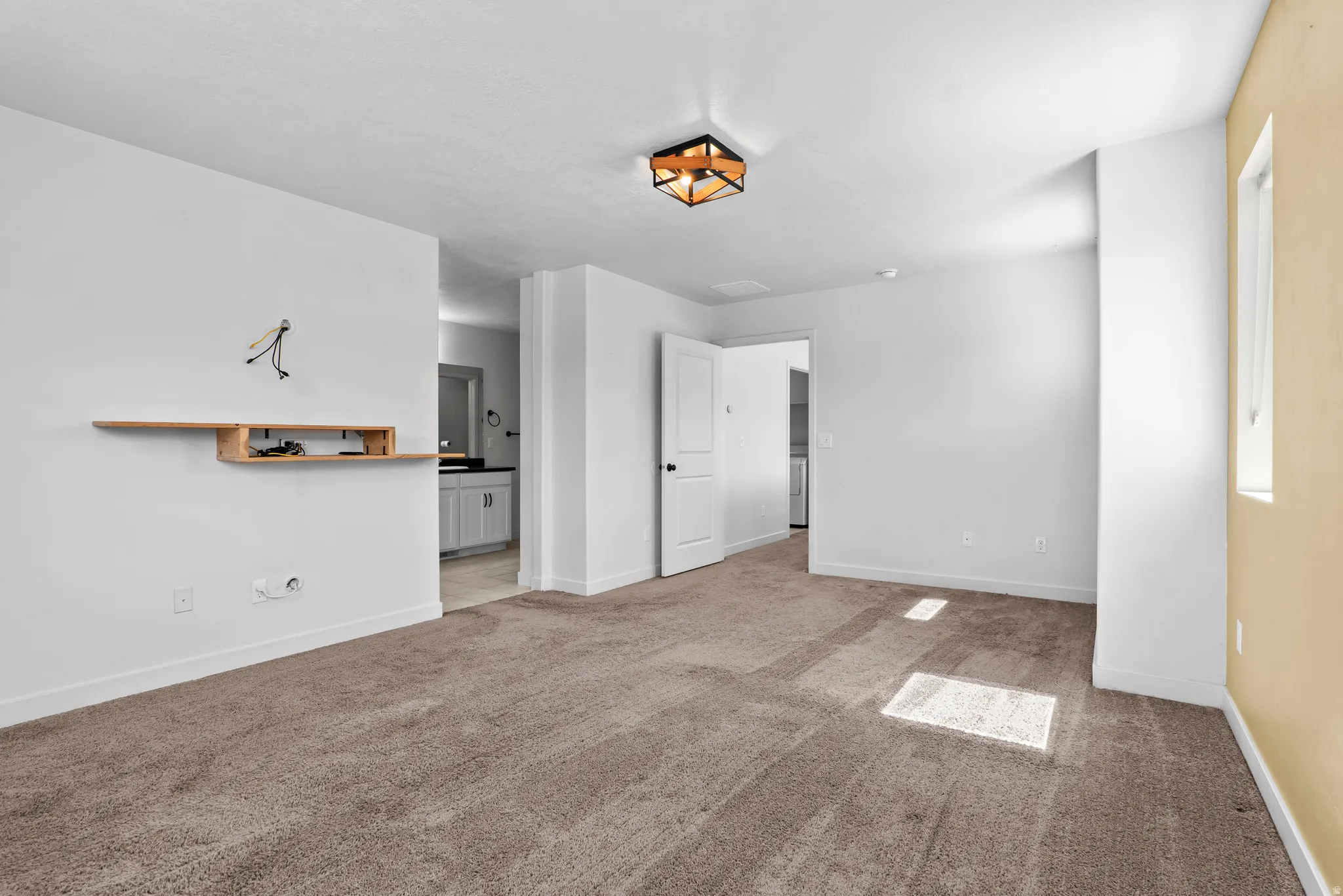 Carpeted room featuring a modern ceiling light fixture, a built-in wall shelf, and a window providing natural light